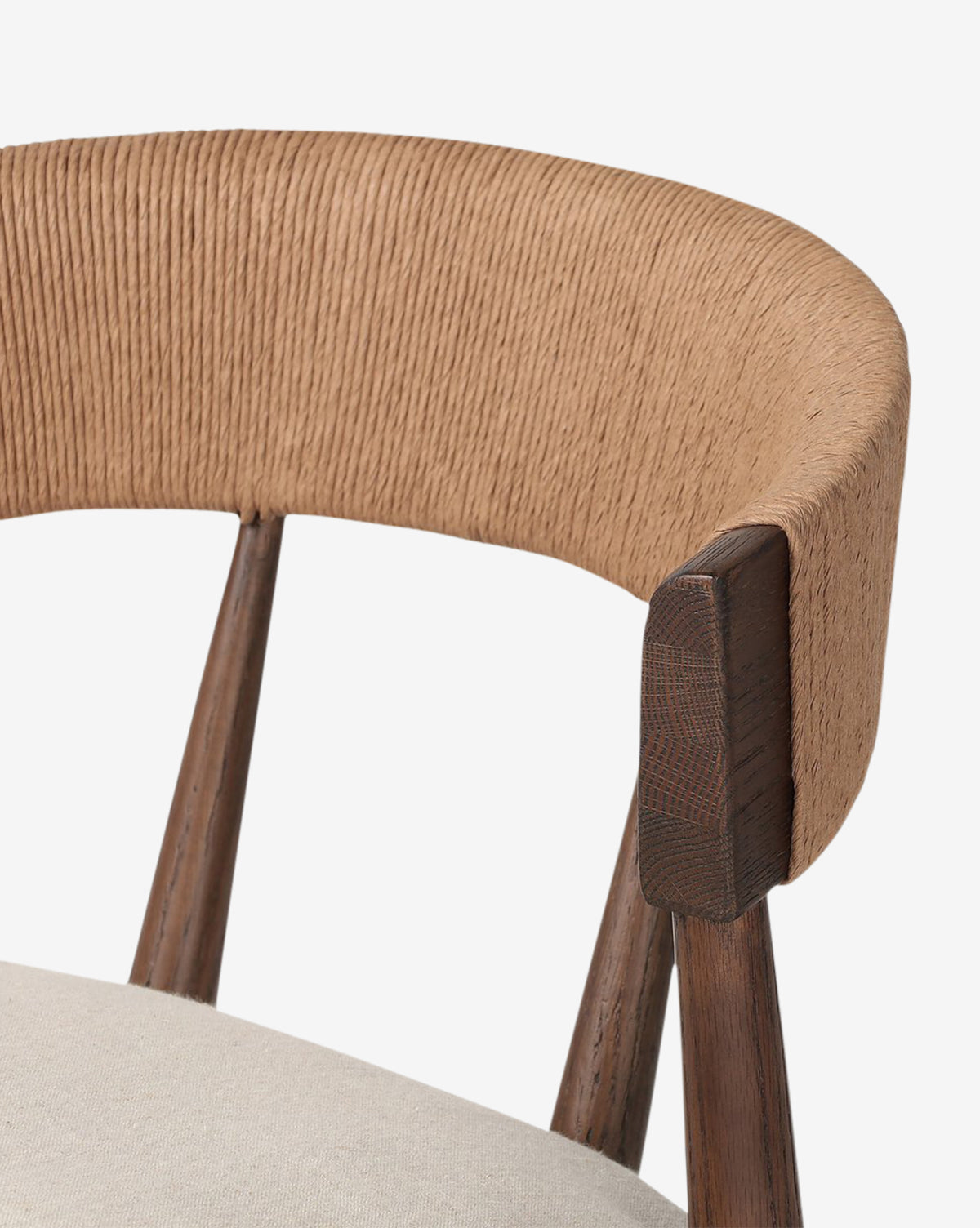 Close-up of the Hallow Chair, featuring a modern rustic design with a curved, light brown woven backrest, dark wooden legs, and a light beige cushioned seat, shown against a plain white background, by McGee & Co.