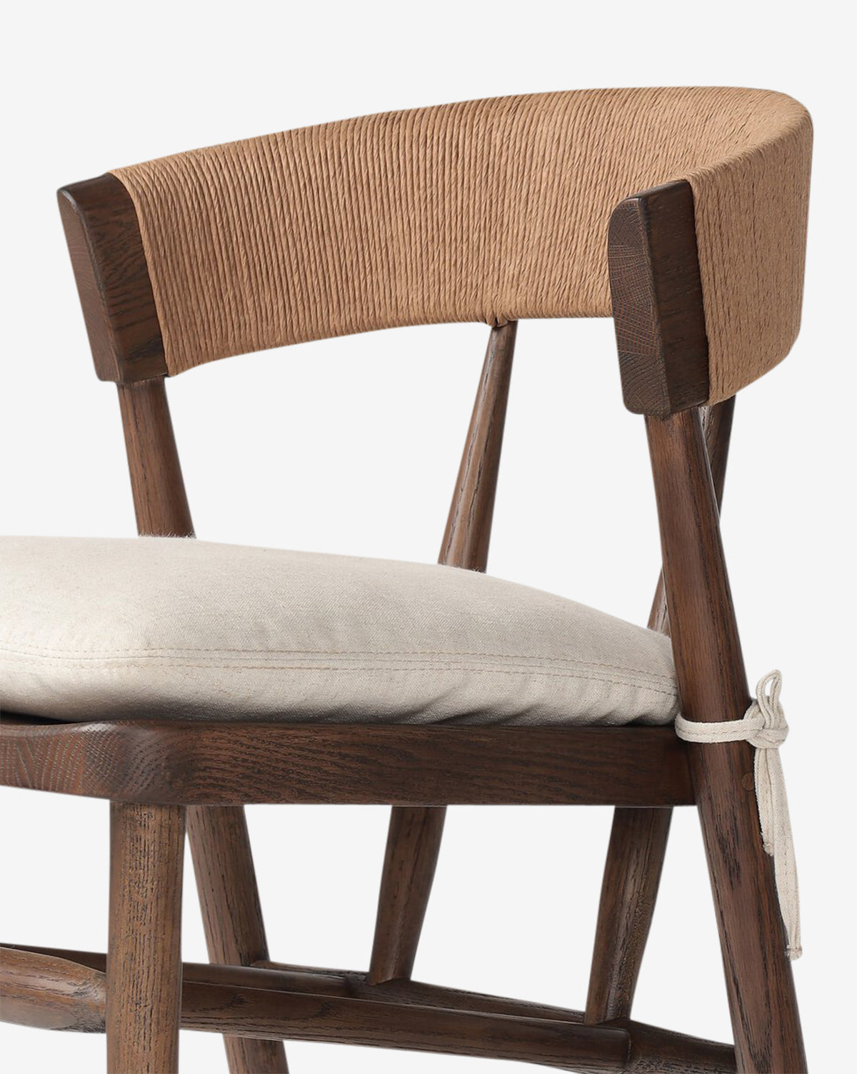 A close-up of the Hallow Chair shows its rustic design with a curved, textured backrest, light cushion tied to the seat, dark wood frame, and sturdy angled legs by McGee & Co.