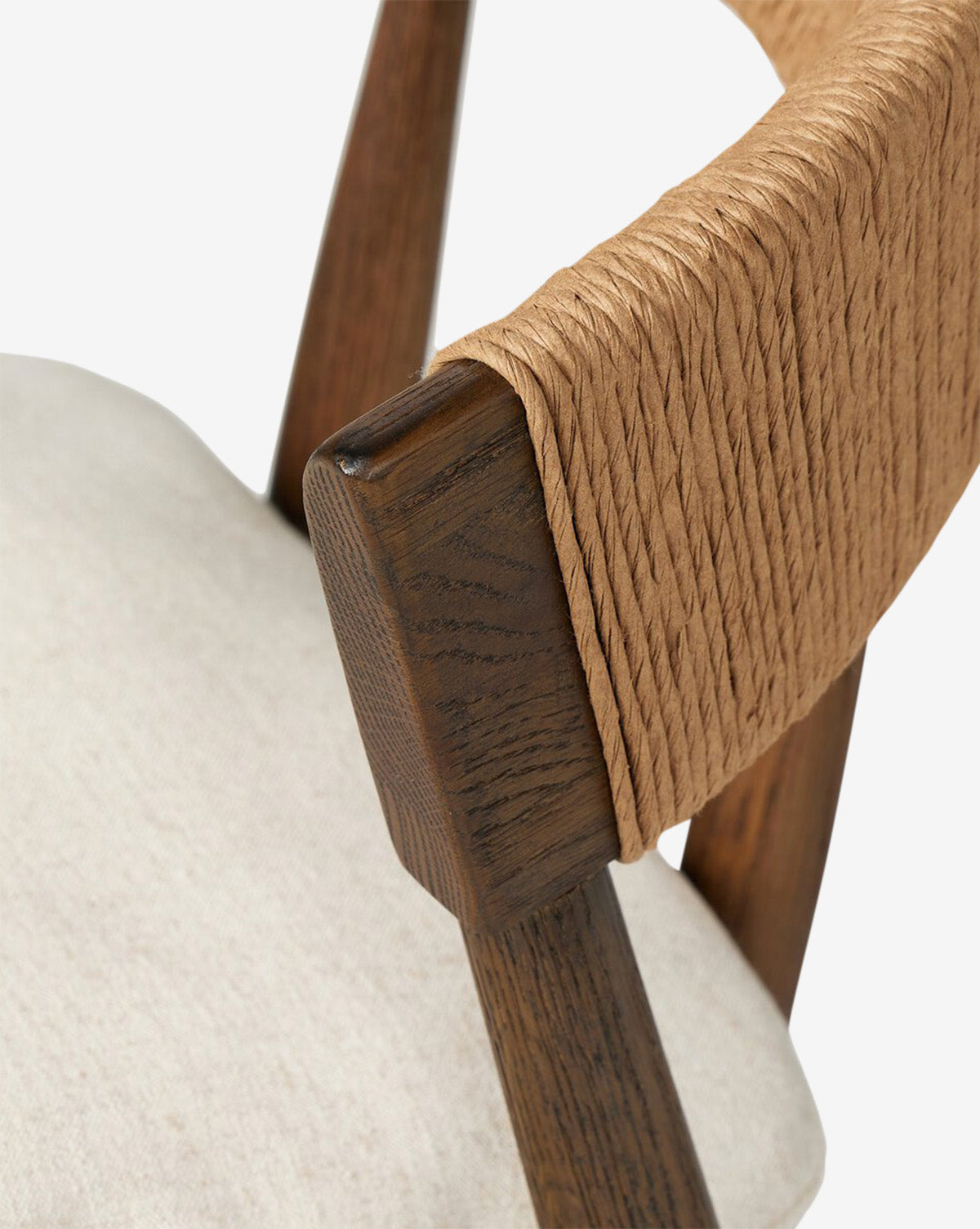 Close-up of the Hallow Chair features a light beige cushion, dark wooden frame, and a curved backrest wrapped with woven natural fiber. The image emphasizes the texture and craftsmanship of this stylish paper rush chair by McGee & Co.