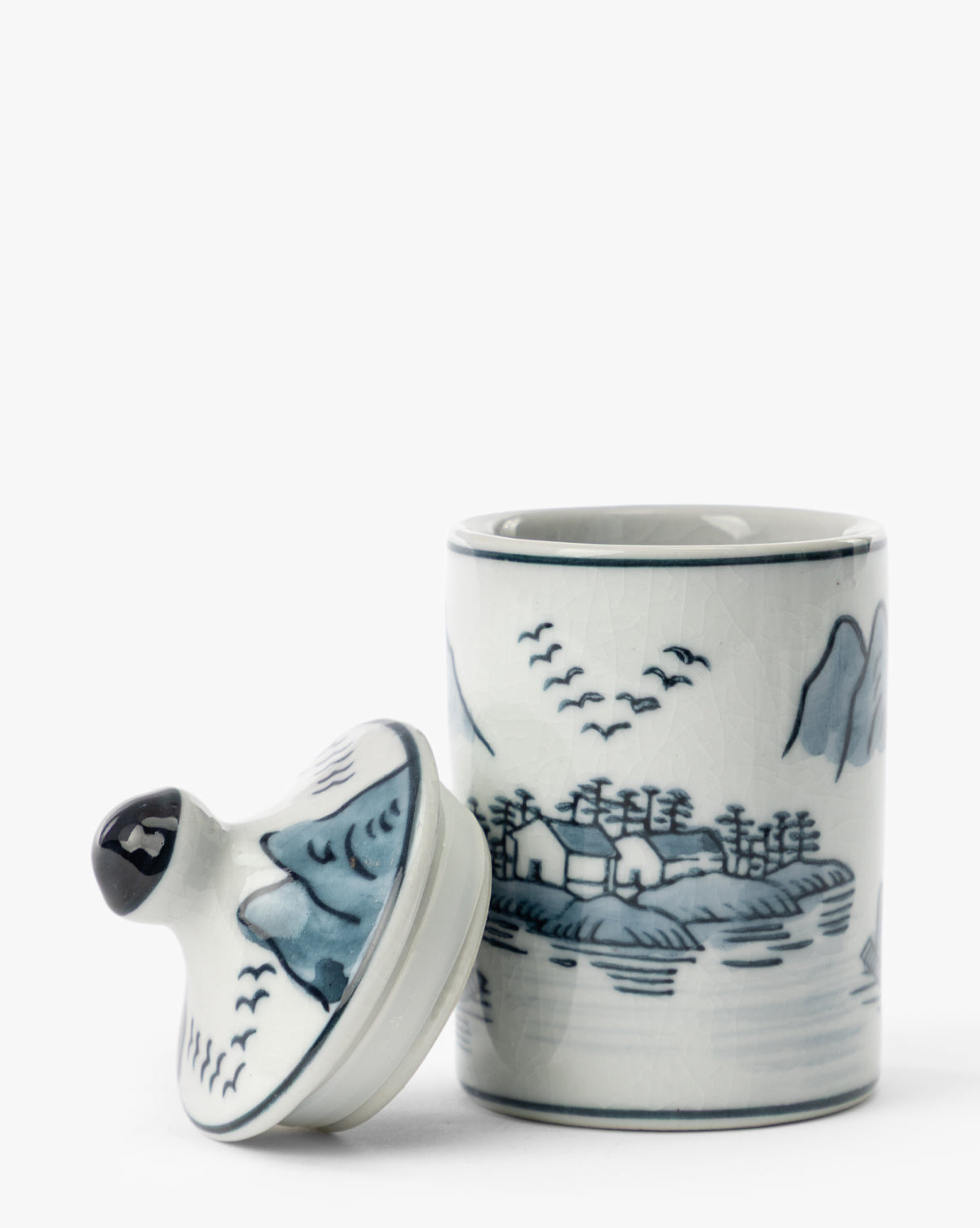 The Hand-Painted Spice Jars (Set of 4) feature blue and white scenic landscapes with trees, mountains, birds, and water. Each ceramic jar includes a lid that can be removed to reveal the open top—perfect as unique artisanal kitchen decor by McGee & Co.