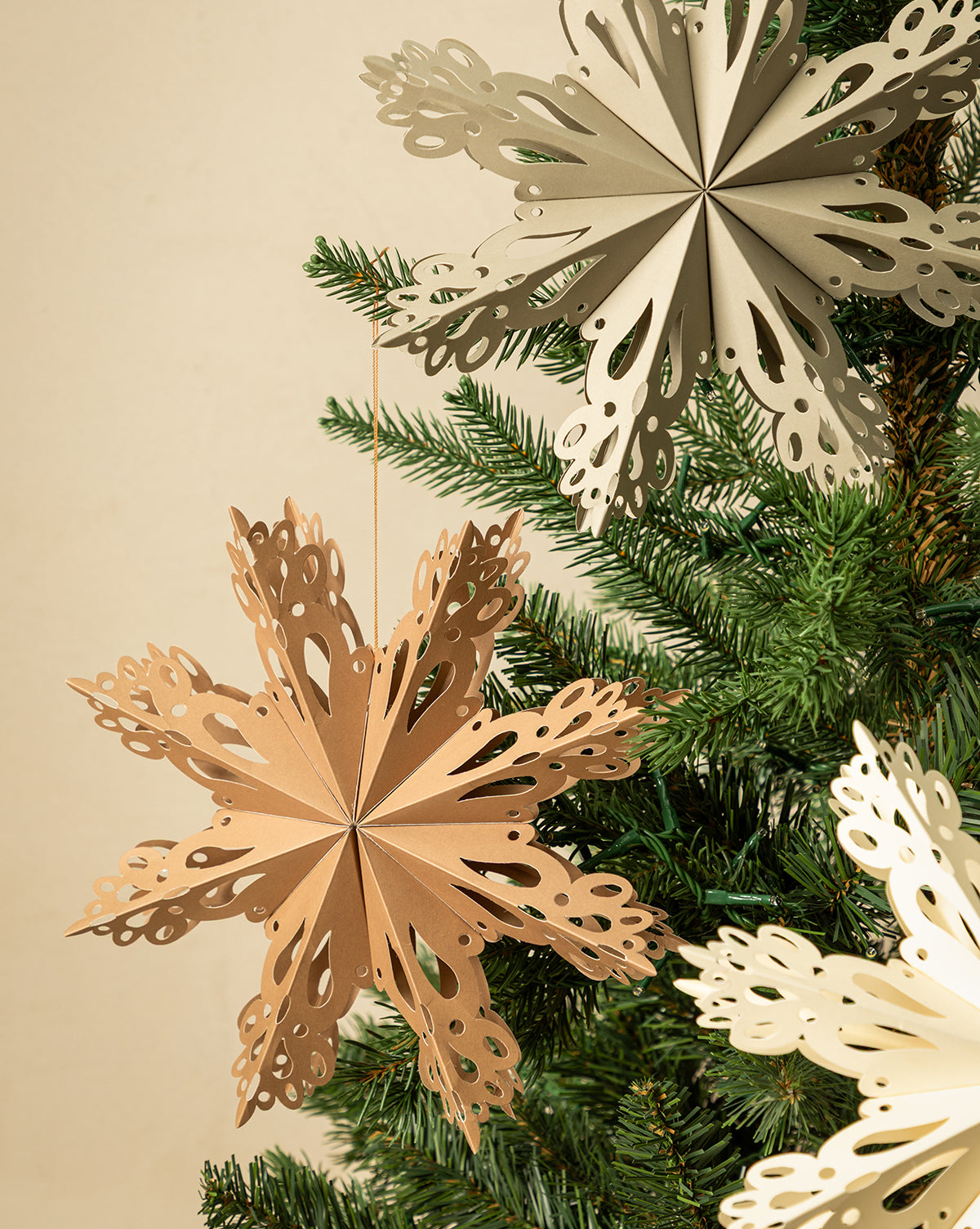 Handmade Assorted Recycled Paper Snowflakes (Set of 3) in neutral beige and cream hang from a green Christmas tree, adding eco-friendly style to your holiday décor against a light background, by McGee & Co.