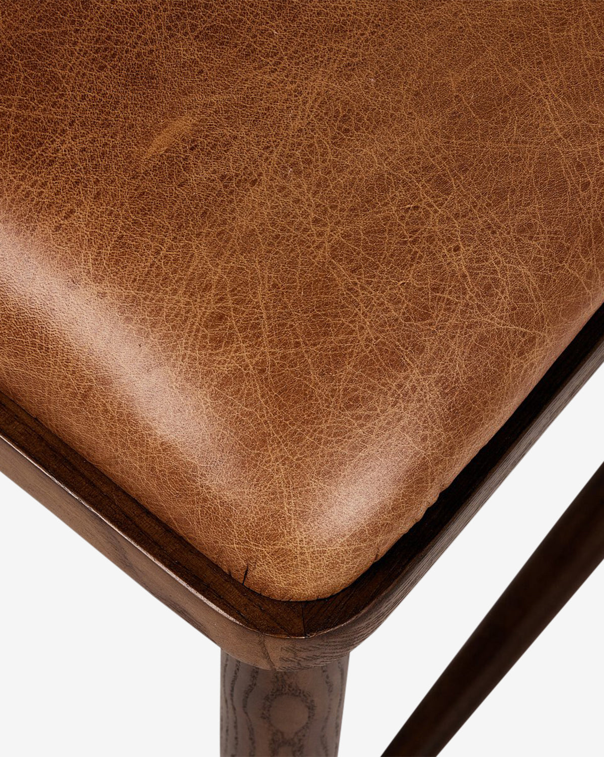 Close-up of the Harper Dining Chairs cushioned seat in brown leather with detailed stitching, set on a solid ash wood frame, shown against a plain white background by McGee & Co.