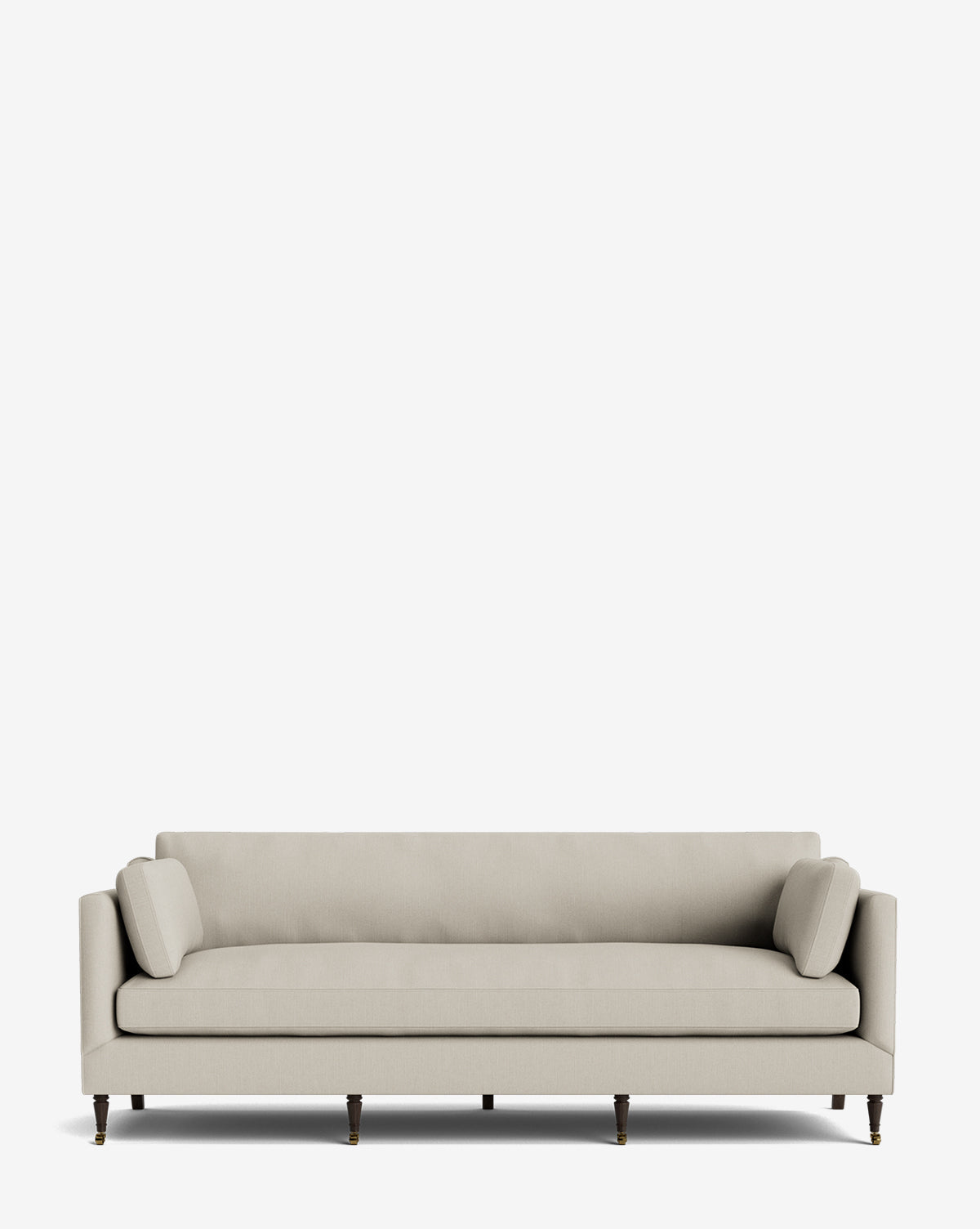 The Haverford Upholstered Sofa 90 is a modern beige handcrafted sofa featuring slim arms, two matching bolster pillows, and wooden legs with brass castors, shown against a plain white background by McGee & Co.