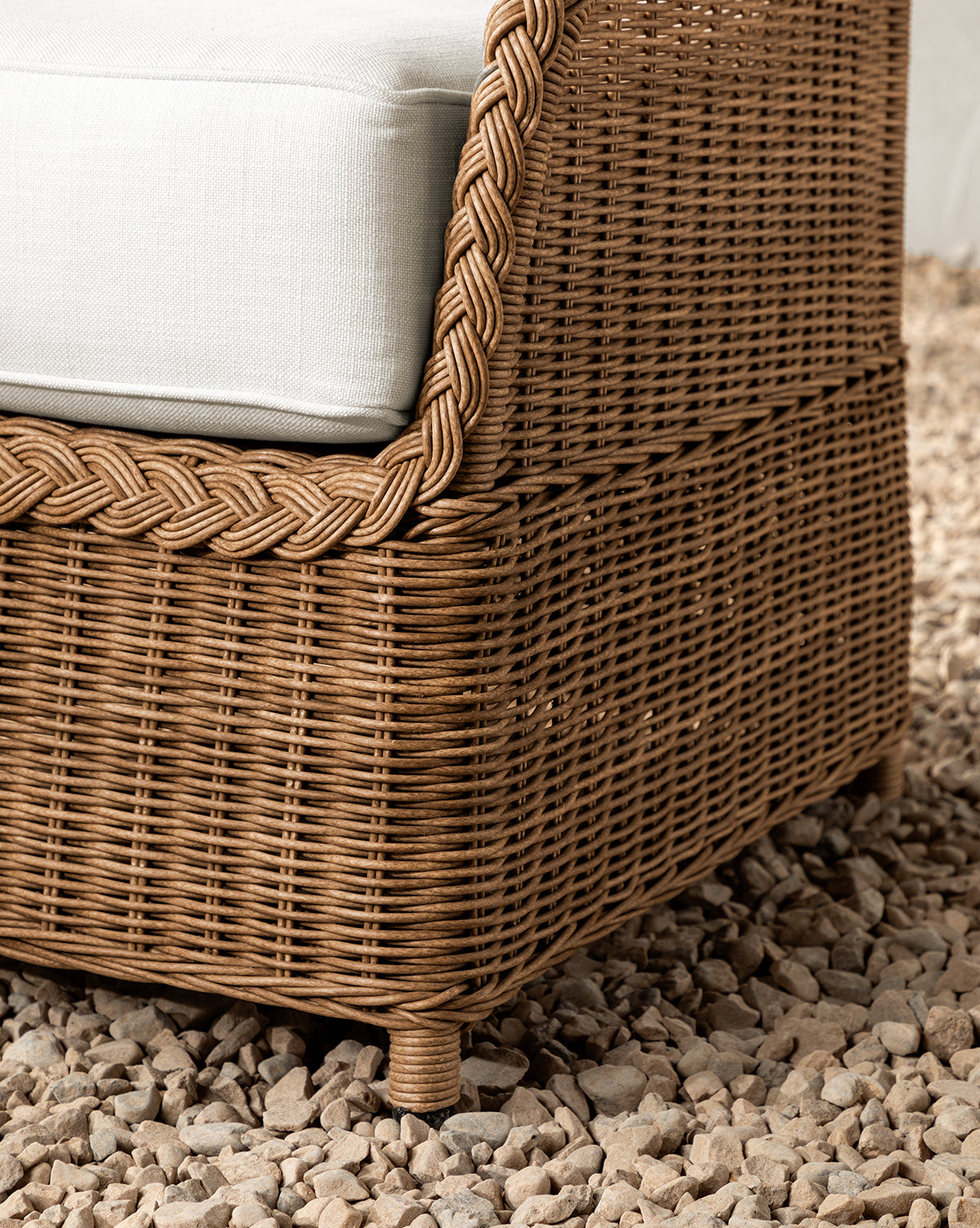 Close-up of the weather-resistant Haviland Outdoor Dining Chair, featuring a braided edge and white cushion, set on light-colored pebbles, by McGee & Co.