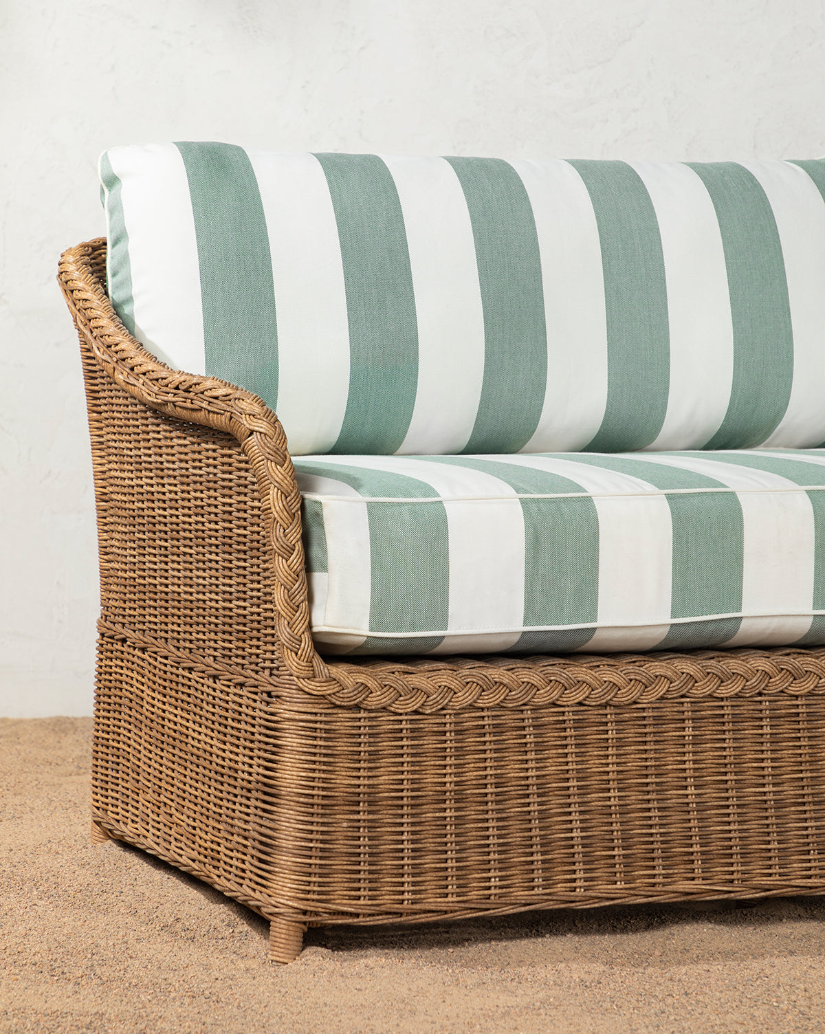 The Haviland Outdoor Sofa with Striped Cushions 88 sits on a pebble floor against a textured white wall, while a potted plant to the right and soft shadows complete this tranquil outdoor setting, by McGee & Co.
