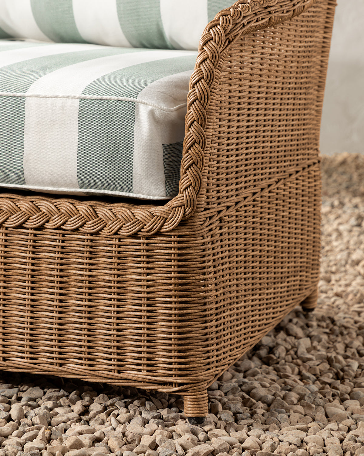 Close-up of the Haviland Outdoor Sofa with Striped Cushions 88, showcasing its braided wicker edges and wide green-and-white striped cushions, set on a bed of small, light-colored rocks by McGee & Co.
