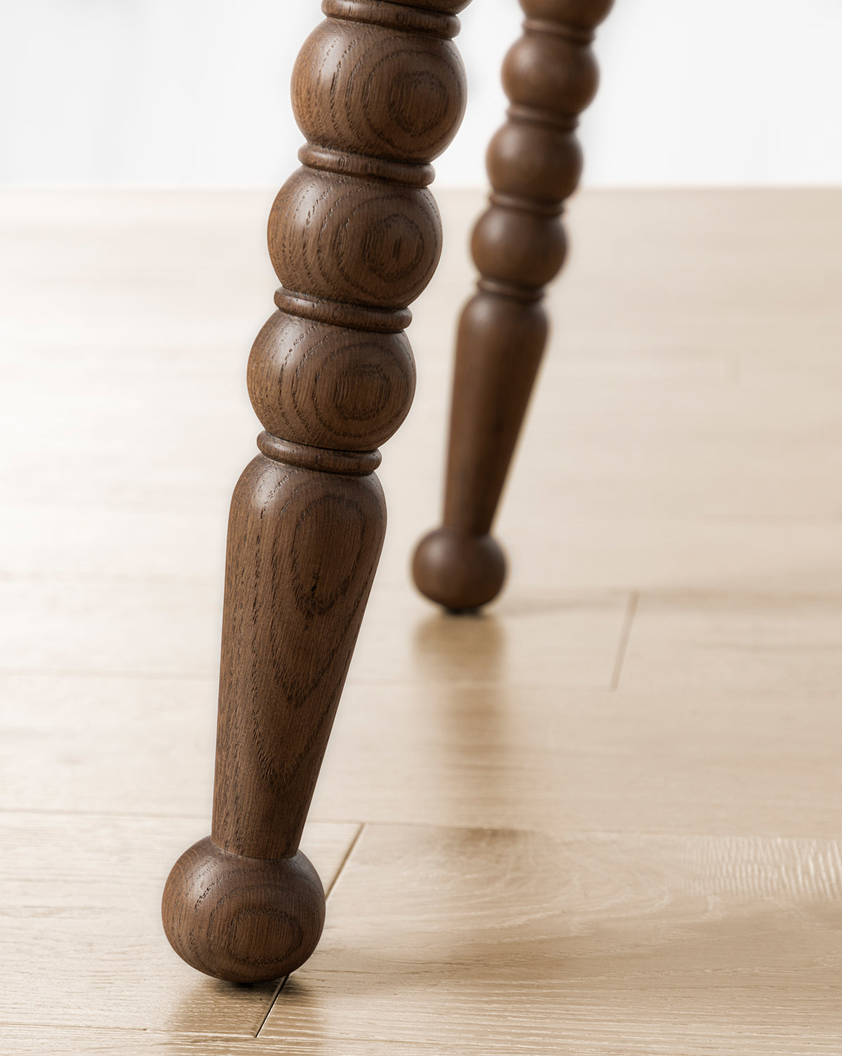 Close-up of two Heathcliff Desk bobbin-style legs with rounded, carved detailing and smooth finish on a light wooden floor. The circular base adds elegance, making it ideal for a stylish home office, by McGee & Co.