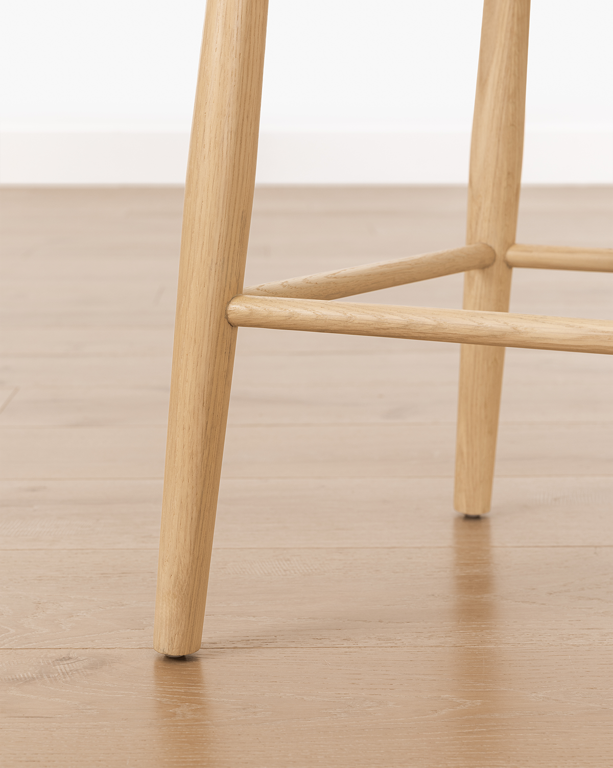 Close-up of Hemingway Chair solid wood legs on a light brown wood floor, with a white wall in the background, by McGee & Co.