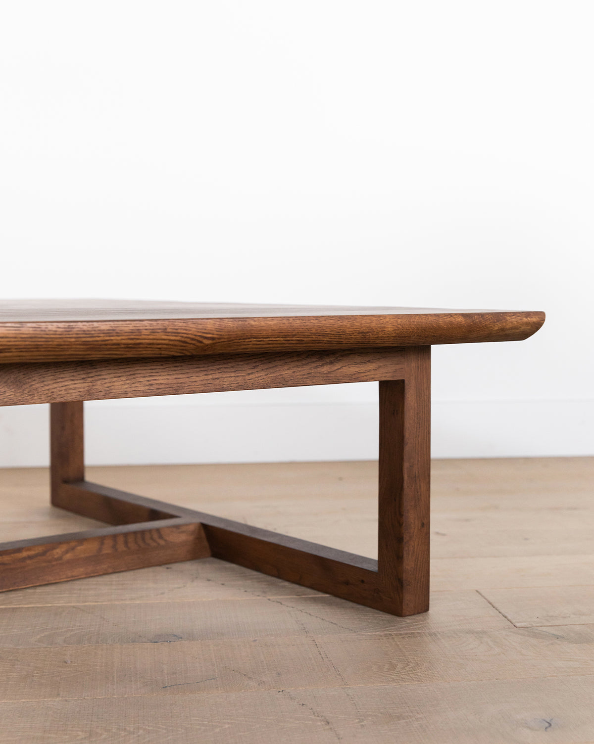 A close-up of the Herrin Coffee Table, featuring a robust solid oak rectangular top and geometric base, set on a light wood floor before a white wall, by McGee & Co.