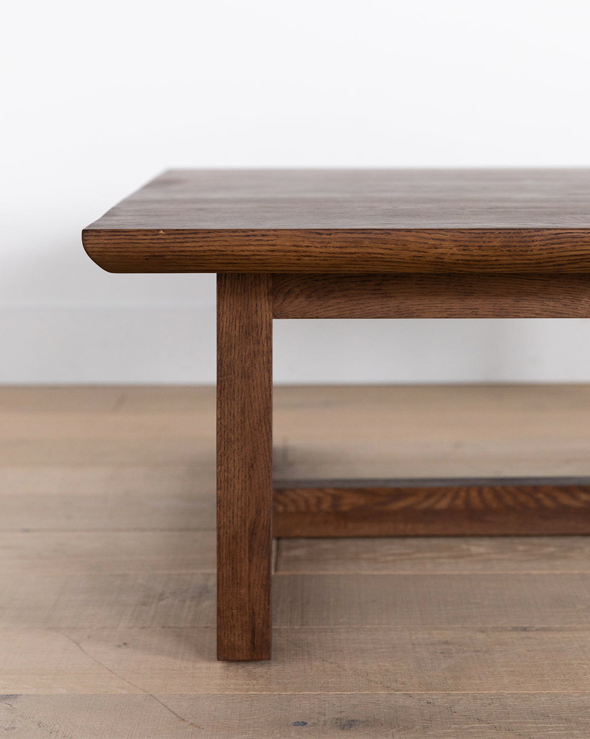 A close-up of the Herrin Coffee Table shows its smooth rectangular top and sturdy legs, set on a light wood floor with a white wall in the background, by McGee & Co.
