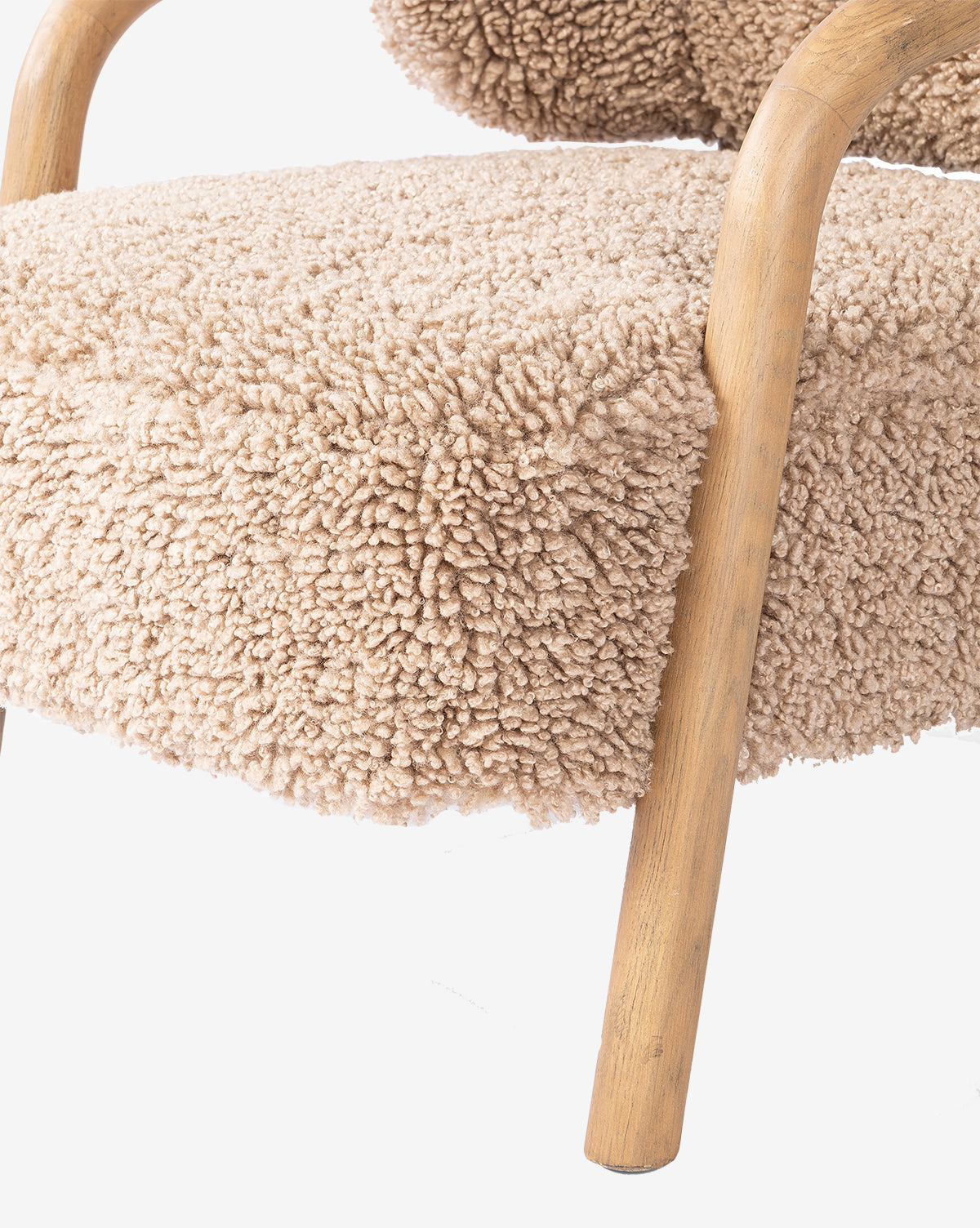 Close-up of the Holstein Lounge Chair, featuring light brown wooden legs and armrests, a solid oak frame, and seat and backrest upholstered in soft, beige, textured boucle fabric by McGee & Co.