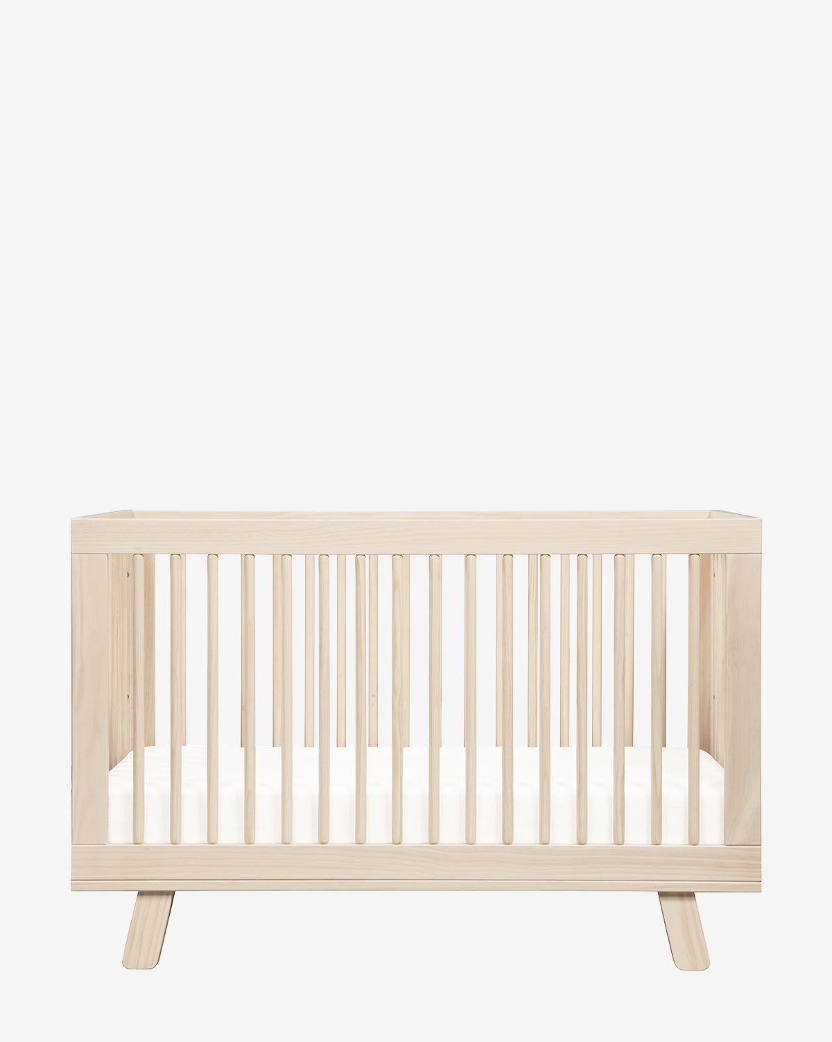 The Hudson Convertible Crib with Toddler Bed Conversion Kit is shown in light wood with vertical slats, a white mattress, modern lines, and angled legs against a plain white background, by McGee & Co.