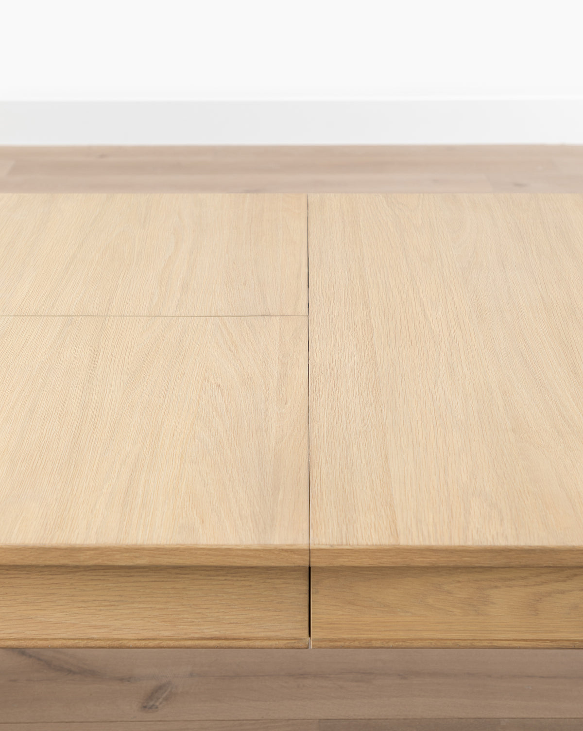Close-up view of the Hughes Oak Extension Dining Table featuring clean lines and a subtle central seam, set on a wooden floor against a white wall, by McGee & Co.