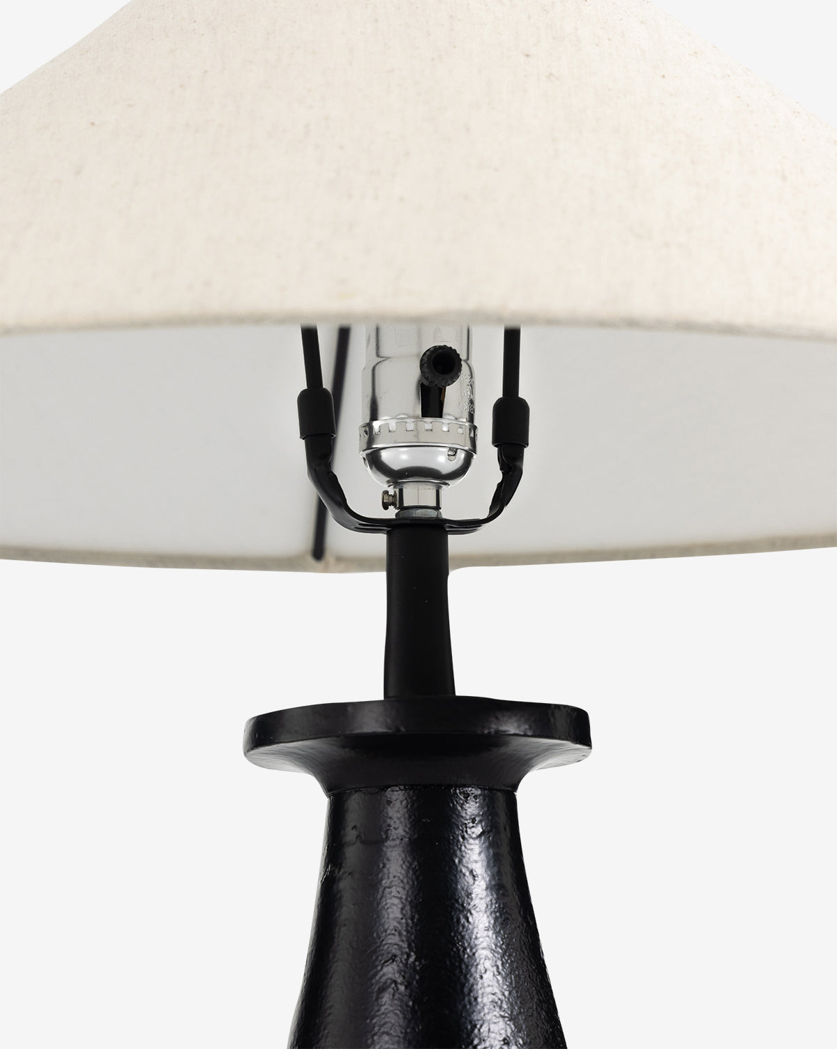 Close-up of the Innes Tapered Table Lamp with a textured black base, silver bulb socket, and beige fabric shade, styled beside a woven abaca mirror for a minimalist look, by McGee & Co.