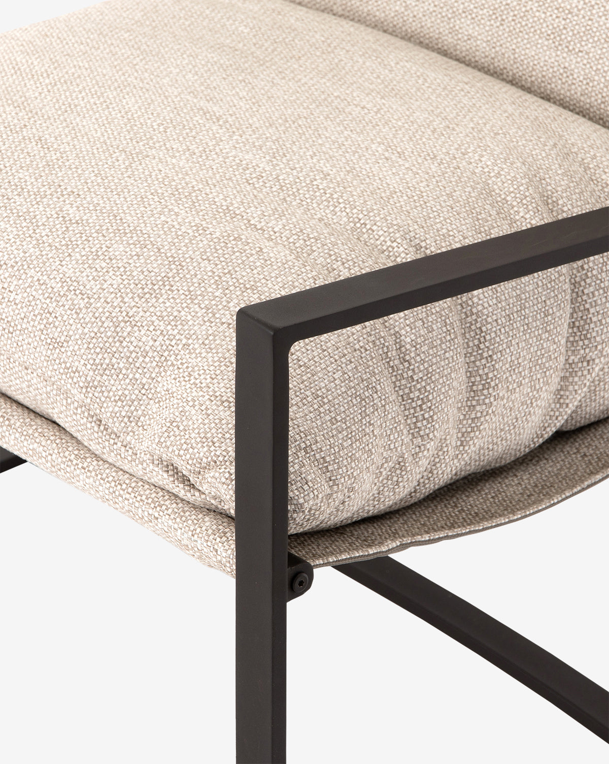Close-up of the Ismay Sling Chair featuring a textured beige removable cushion and a sleek black metal frame with angular lines, set against a plain white background by McGee & Co.