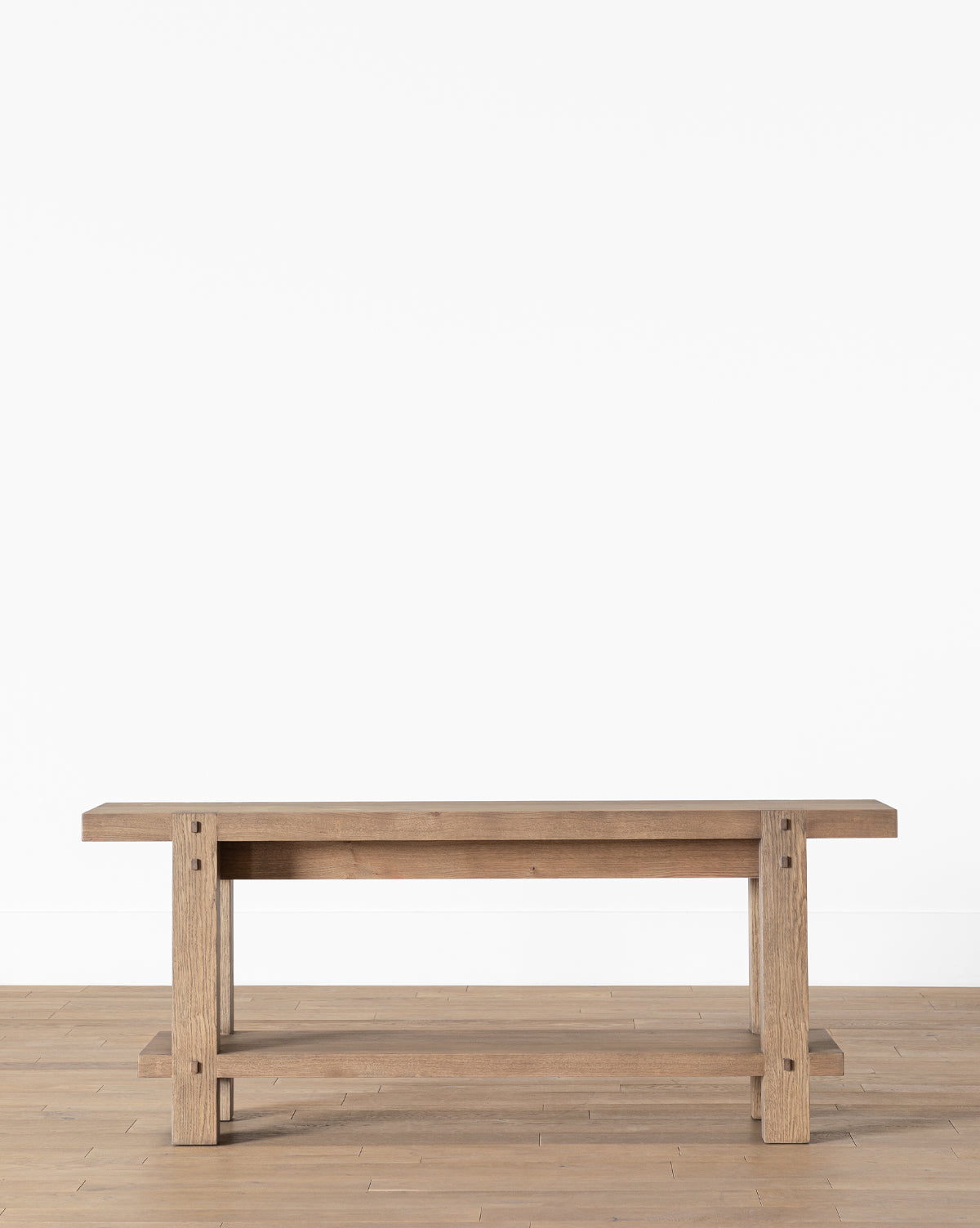 The Jack Console Table features a simple, sturdy design with exposed joinery and a natural wood finish, making it the perfect piece to complement modern farmhouse furniture against a light wood floor and plain white wall, by McGee & Co.