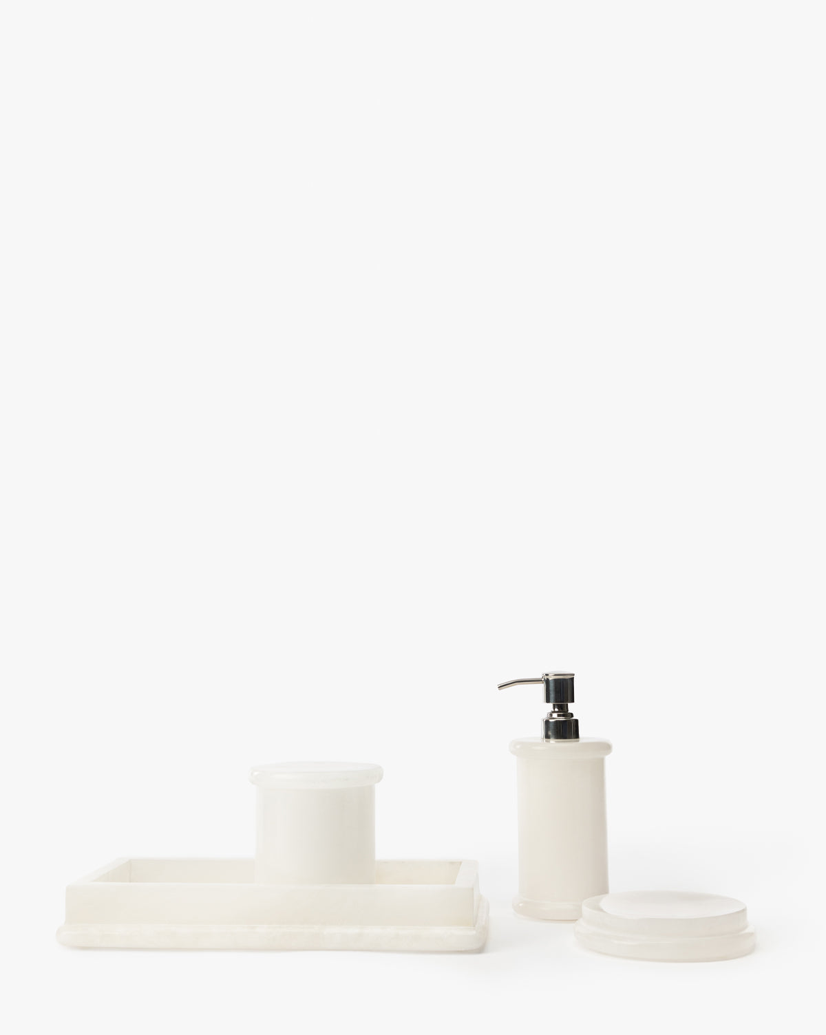 Four alabaster bathroom accessories from the Jennings Bath Collection—a rectangular tray, lidded jar, soap dispenser with black pump, and round container—are displayed on a white surface, ideal for modern bathroom decor by McGee & Co.