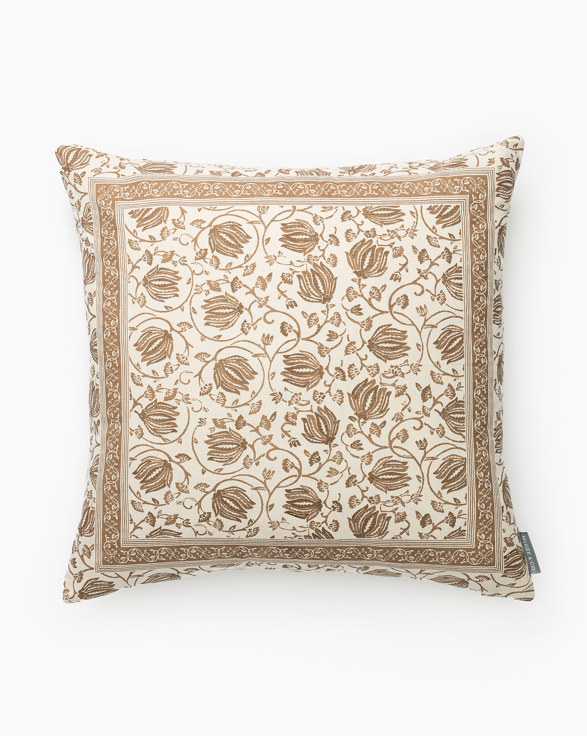 The Jolie Floral Pillow Cover features an intricate brown floral and leaf design with a detailed border on a cream background, all in a muted palette. A fabric tag is sewn into the lower right side for added detail, by McGee & Co.