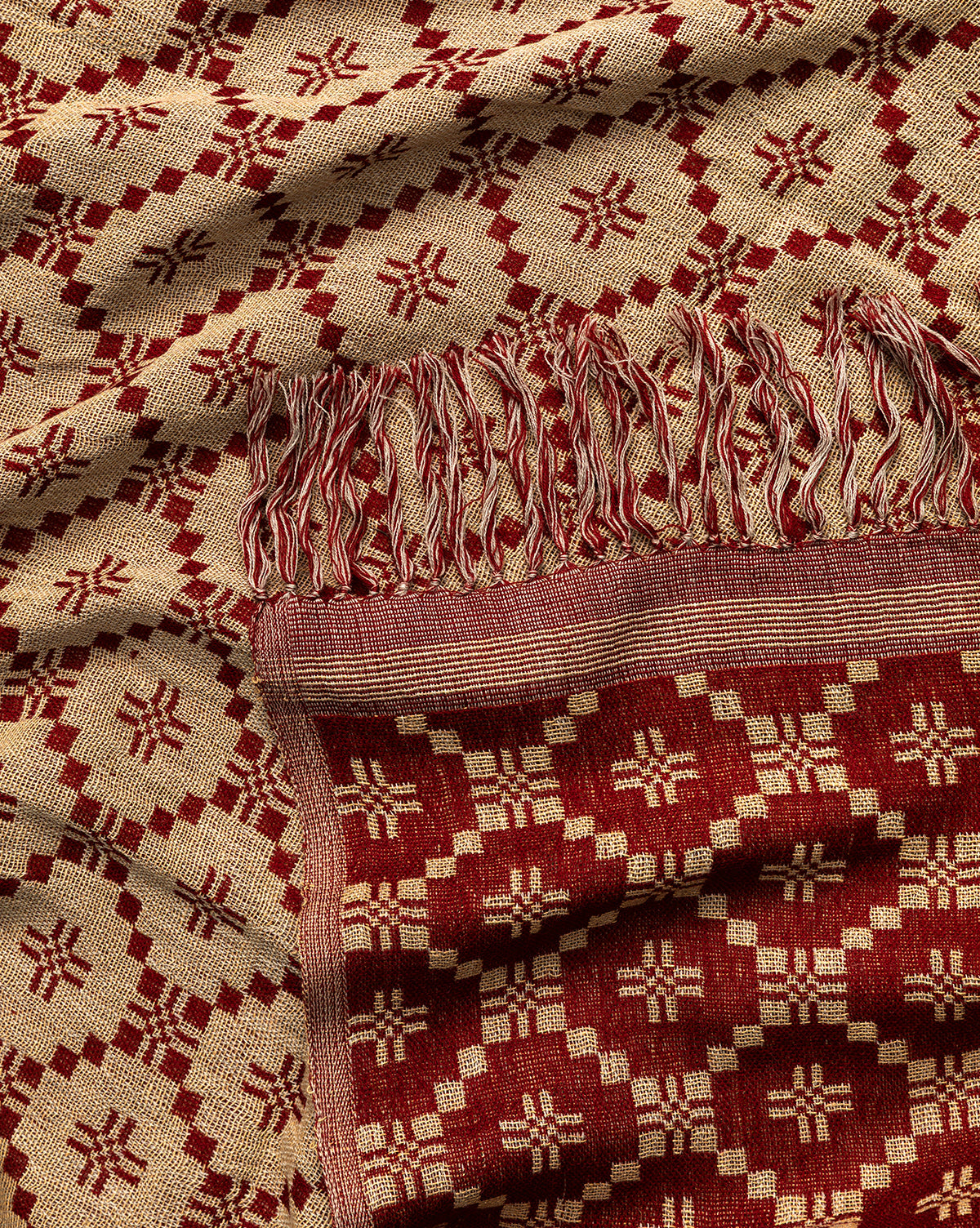 A close-up of the Jude Reversible Woven Throw, showcasing its vintage-inspired red and beige geometric pattern, fringed edges, and intricate diamond and cross designs that reflect traditional craftsmanship, by McGee & Co.