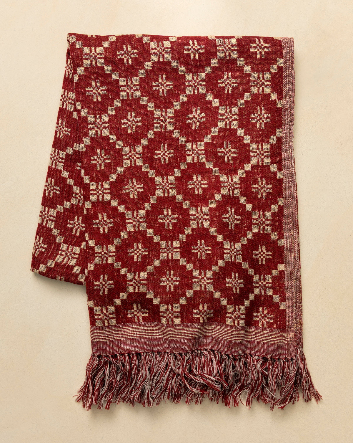 The Jude Reversible Woven Throw features a vintage-inspired red and beige geometric floral pattern with twisted fringe, making it a cozy accent for any light beige surface, by McGee & Co.