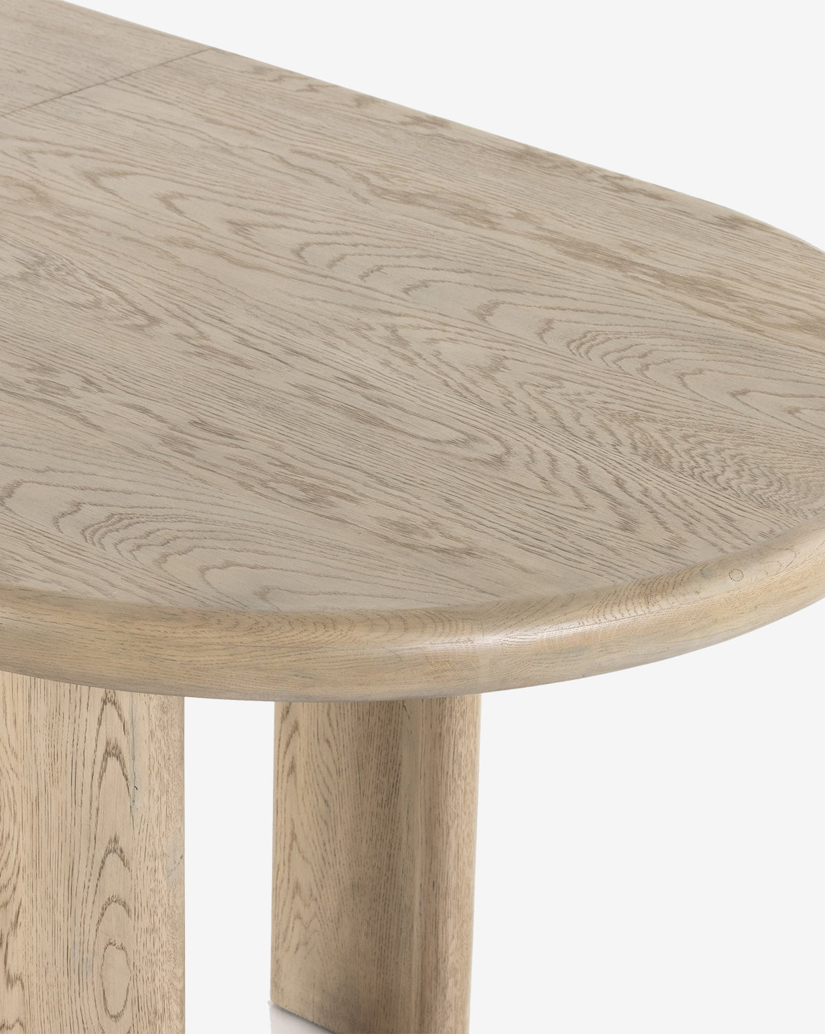 A close-up view of the Juliana Extension Dining Table showcases its solid oak build, natural grain, rounded edges, and sturdy wooden legs, highlighting the modern tabletop design against a white background by McGee & Co.