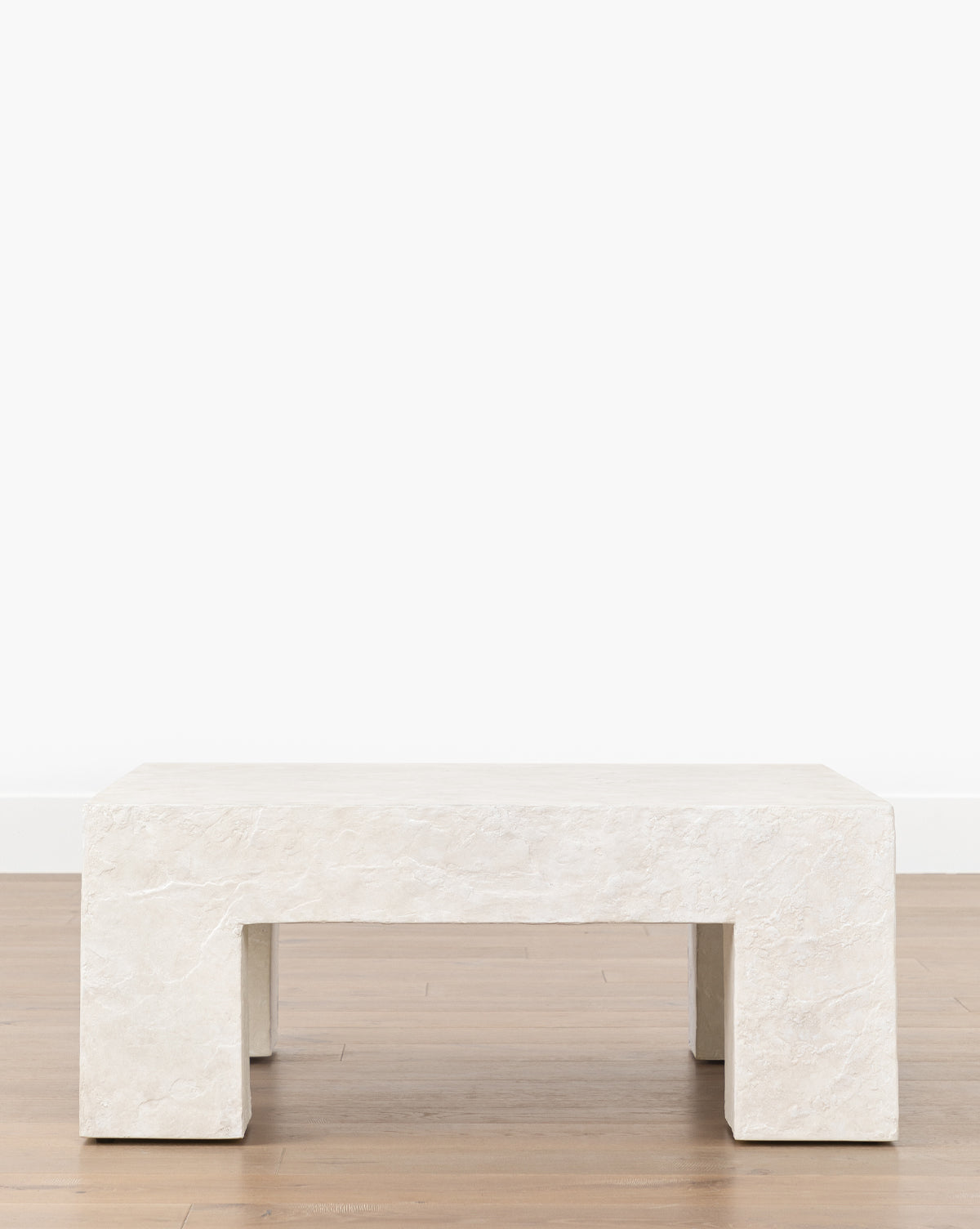 The Julio Coffee Table features a minimalist rectangular design in white stone with thick block legs, set on a light wooden floor against a plain white wall for a sculptural look, by McGee & Co.