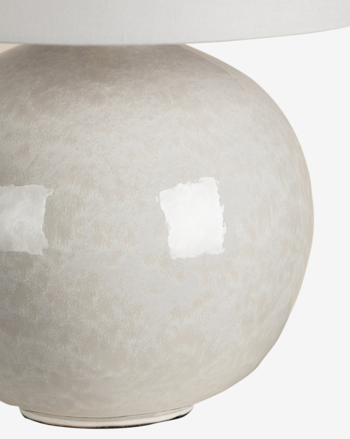 Close-up of the base of the Karina Table Lamp, a round ceramic lamp in light beige with an ivory finish, showcasing a subtle mottled pattern and a reflective white patch by McGee & Co.