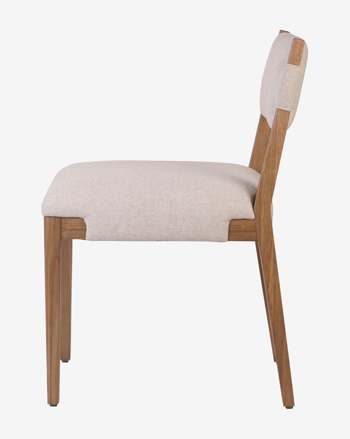 A side view of the Kennebec Dining Chair shows its light beige performance fabric upholstery, ash frame with angled wooden legs, and a padded seat and backrest for comfort, by McGee & Co.