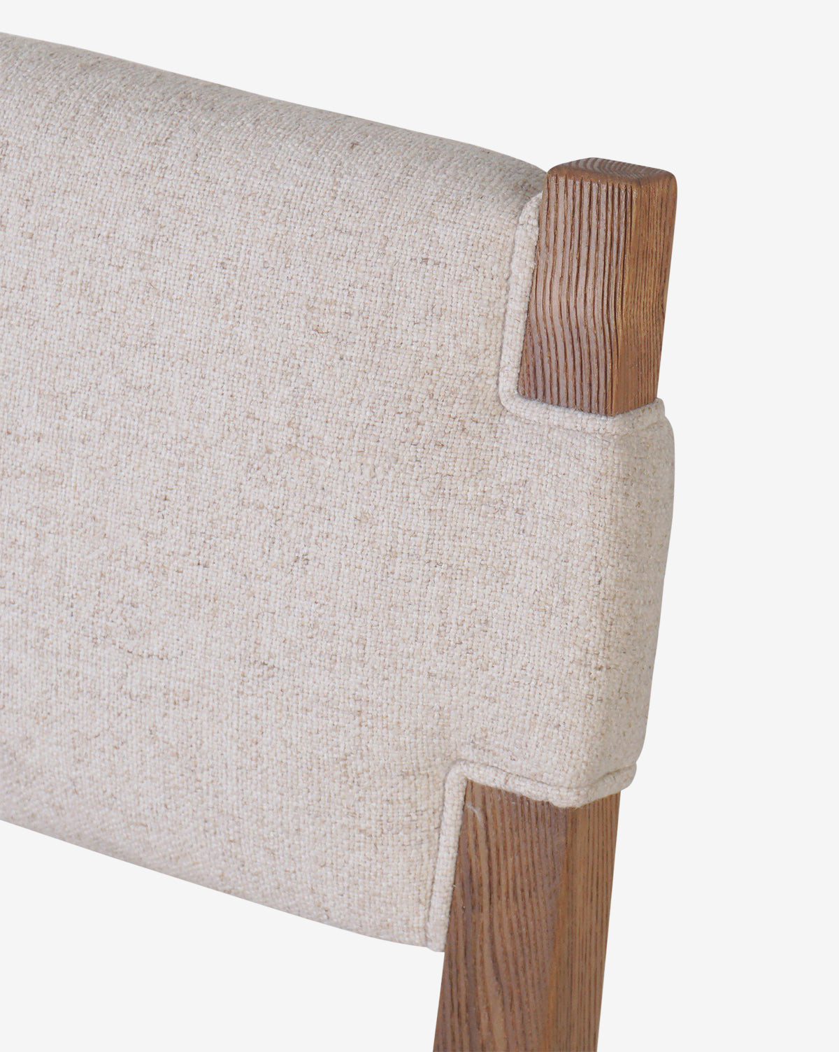Close-up of the Kennebec Dining Chair’s backrest, featuring light beige, textured performance fabric upholstery and an ash frame with a natural wood grain finish, by McGee & Co.