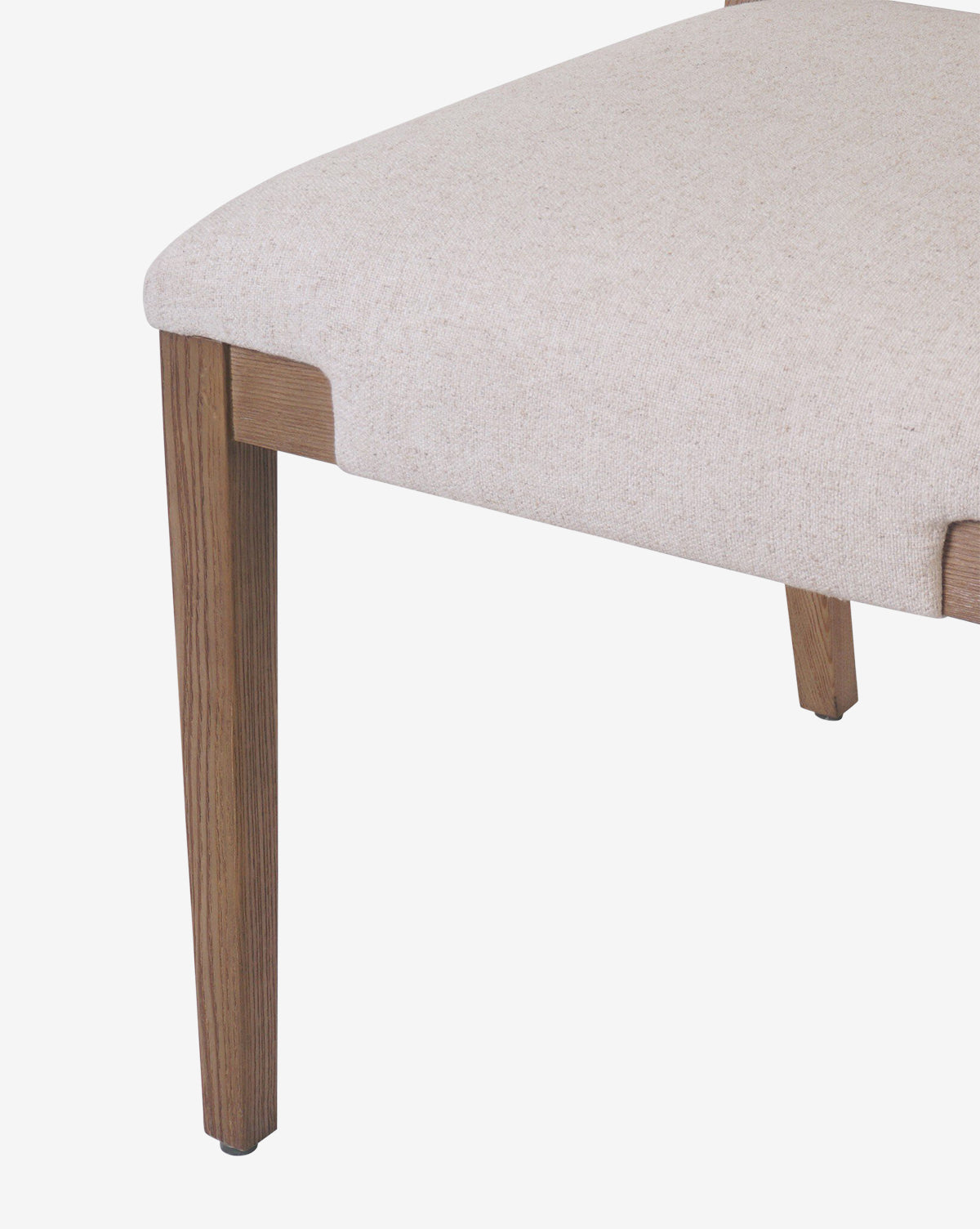 A close-up of the Kennebec Dining Chair showcases its beige upholstery and ash frame, focusing on the seat and one front leg against a white background, by McGee & Co.