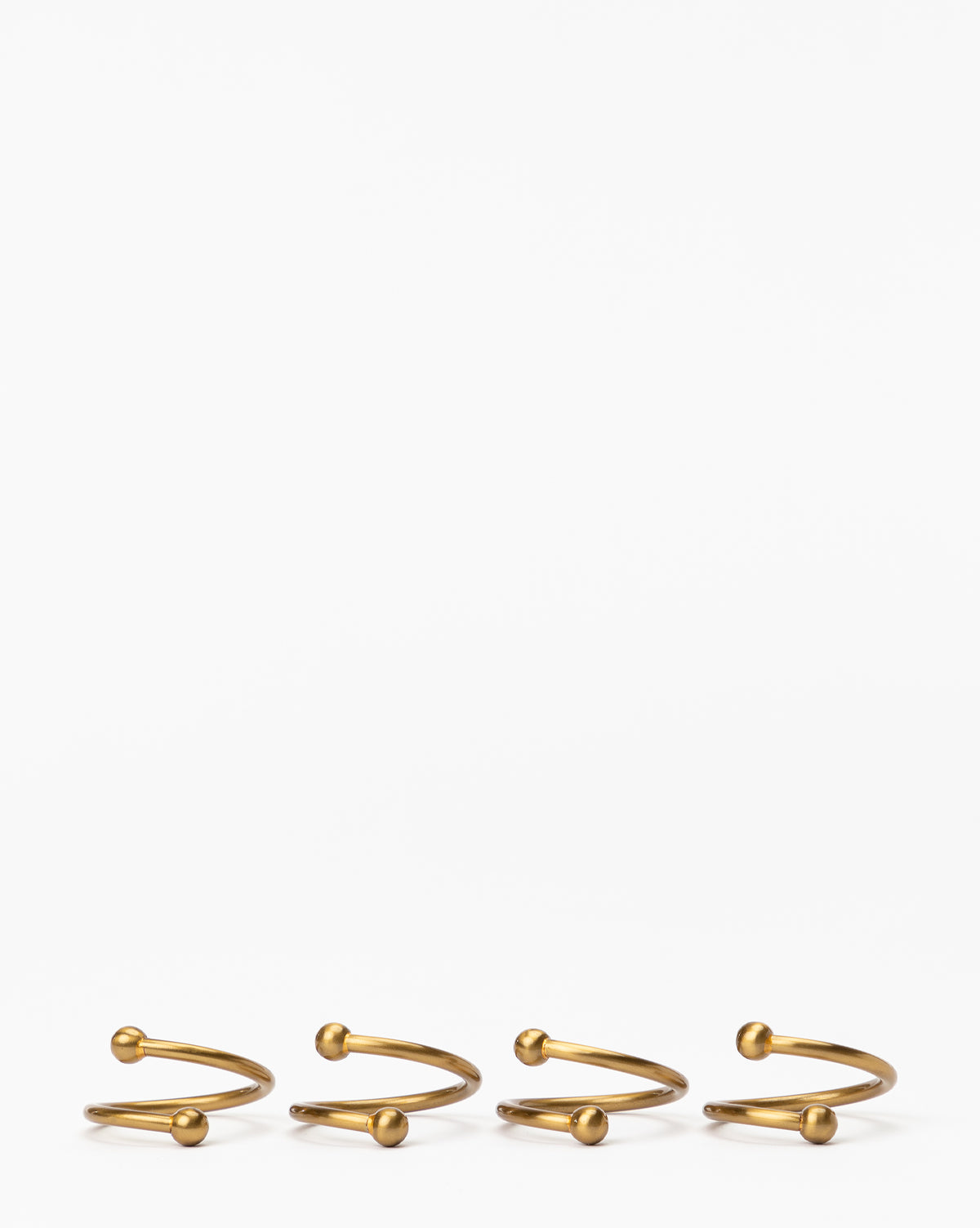 The Kinne Metal Napkin Rings (Set of 4) feature a minimal brass design with small round ends, elegantly displayed side by side on a plain white background—perfect as stylish table setting accessories by McGee & Co.