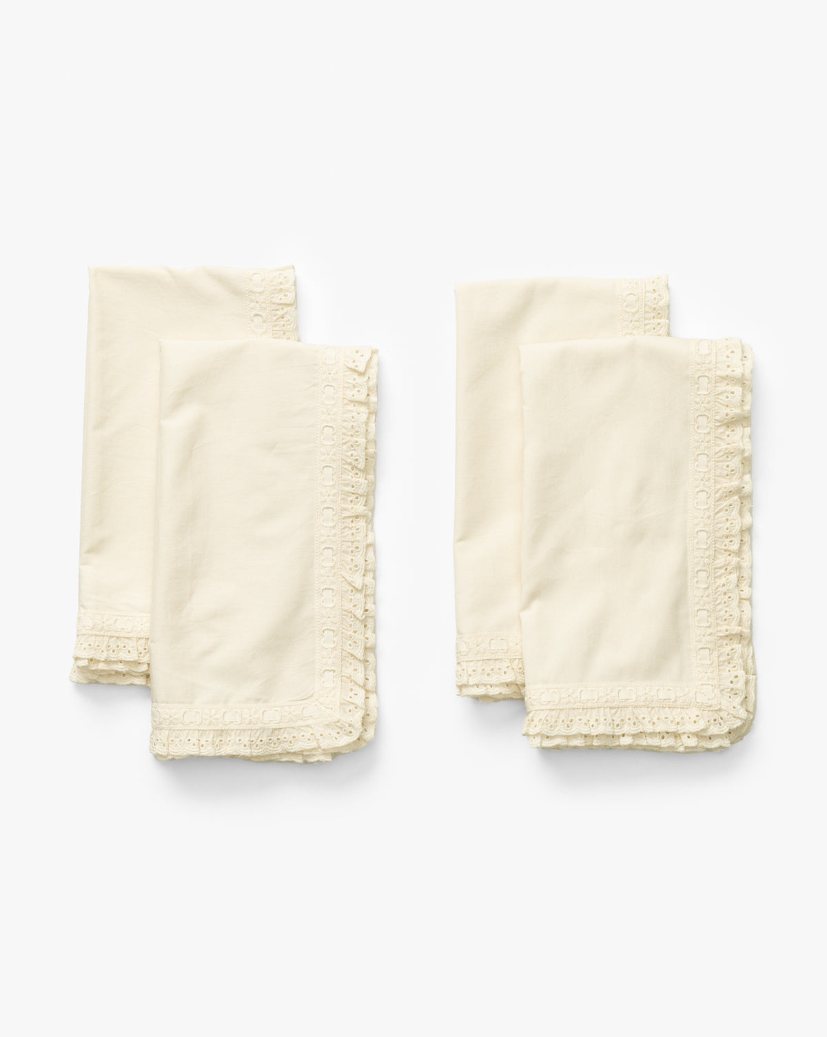 The Lace Trim Napkins (Set of 4) feature cream-colored fabric with decorative borders, elegantly folded and displayed side by side—ideal table linens to add a touch of sophistication to any occasion, by McGee & Co.