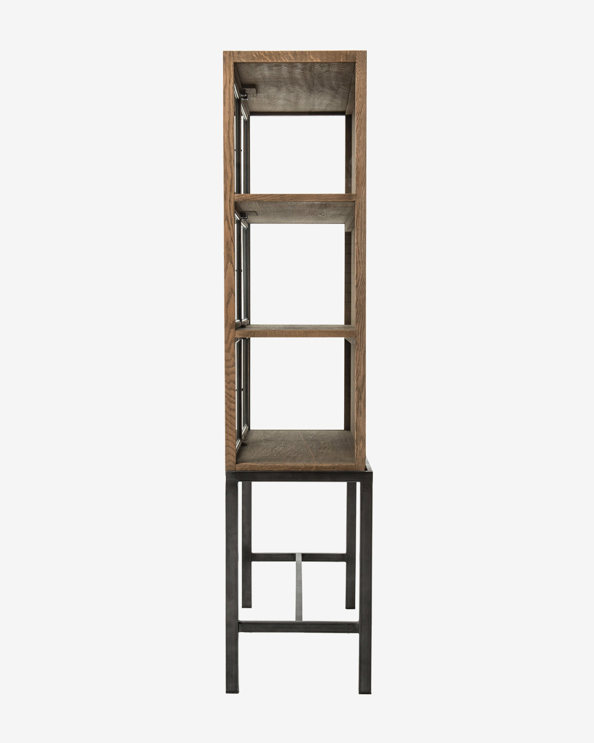 A side view of the Lawley Cabinet, a tall rectangular curio with a drift oak frame, three shelves, and minimalist metal base and legs in an industrial style, by McGee & Co.