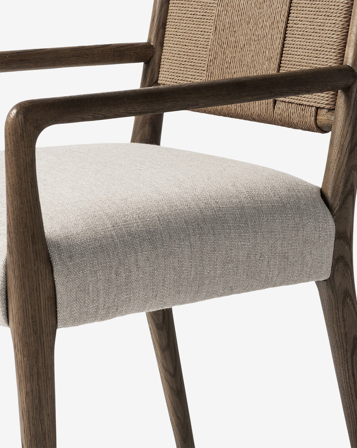 Close-up of the Leola Dining Armchair, crafted from oak with a rush back, light beige upholstered seat, and elegantly curved wooden armrests and legs, shown against a plain white background by McGee & Co.