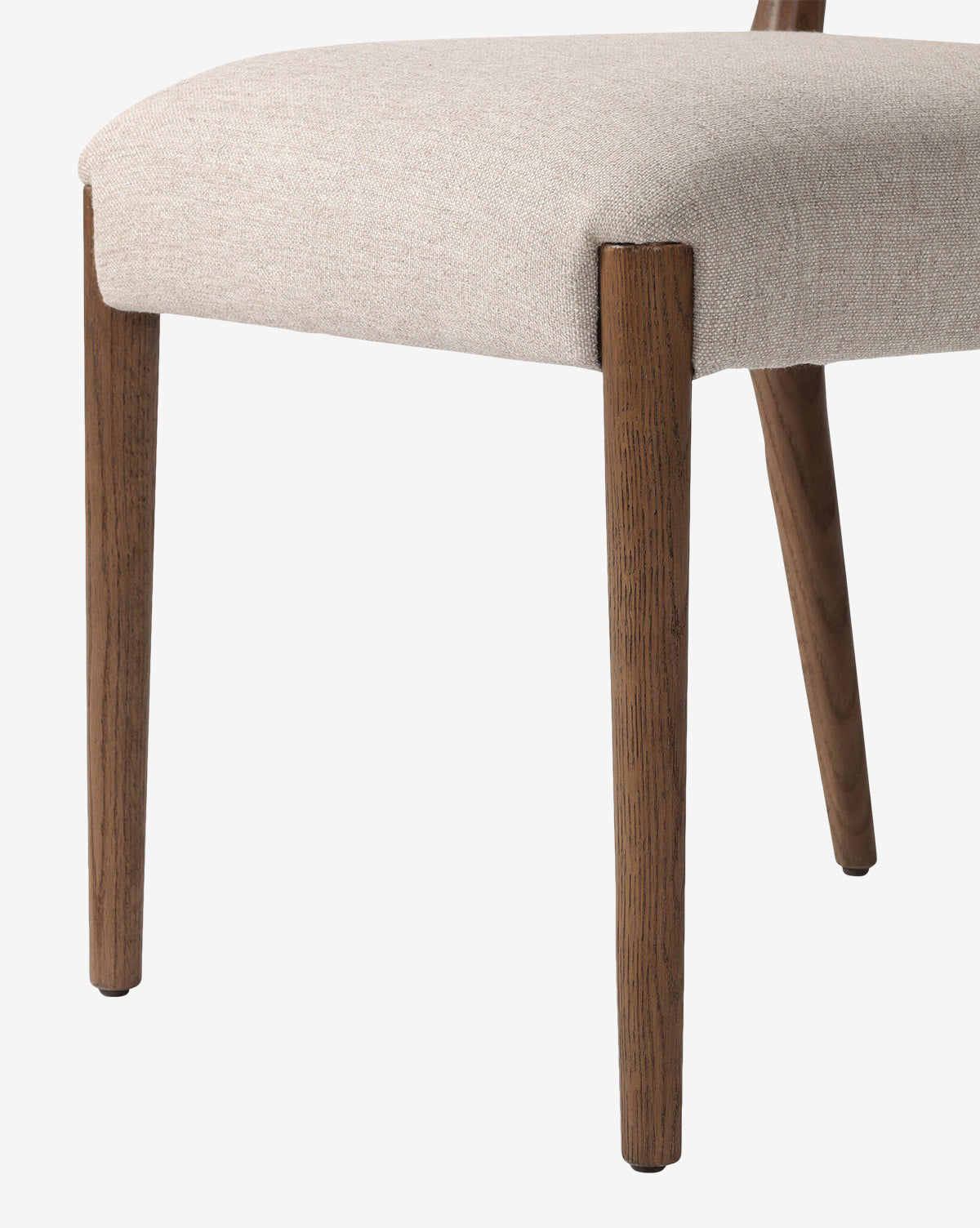 Close-up of the Leola Dining Chair featuring a modern oak frame, light beige upholstered seat, angled wooden legs, and detailed fabric texture with rich wood grain, by McGee & Co.
