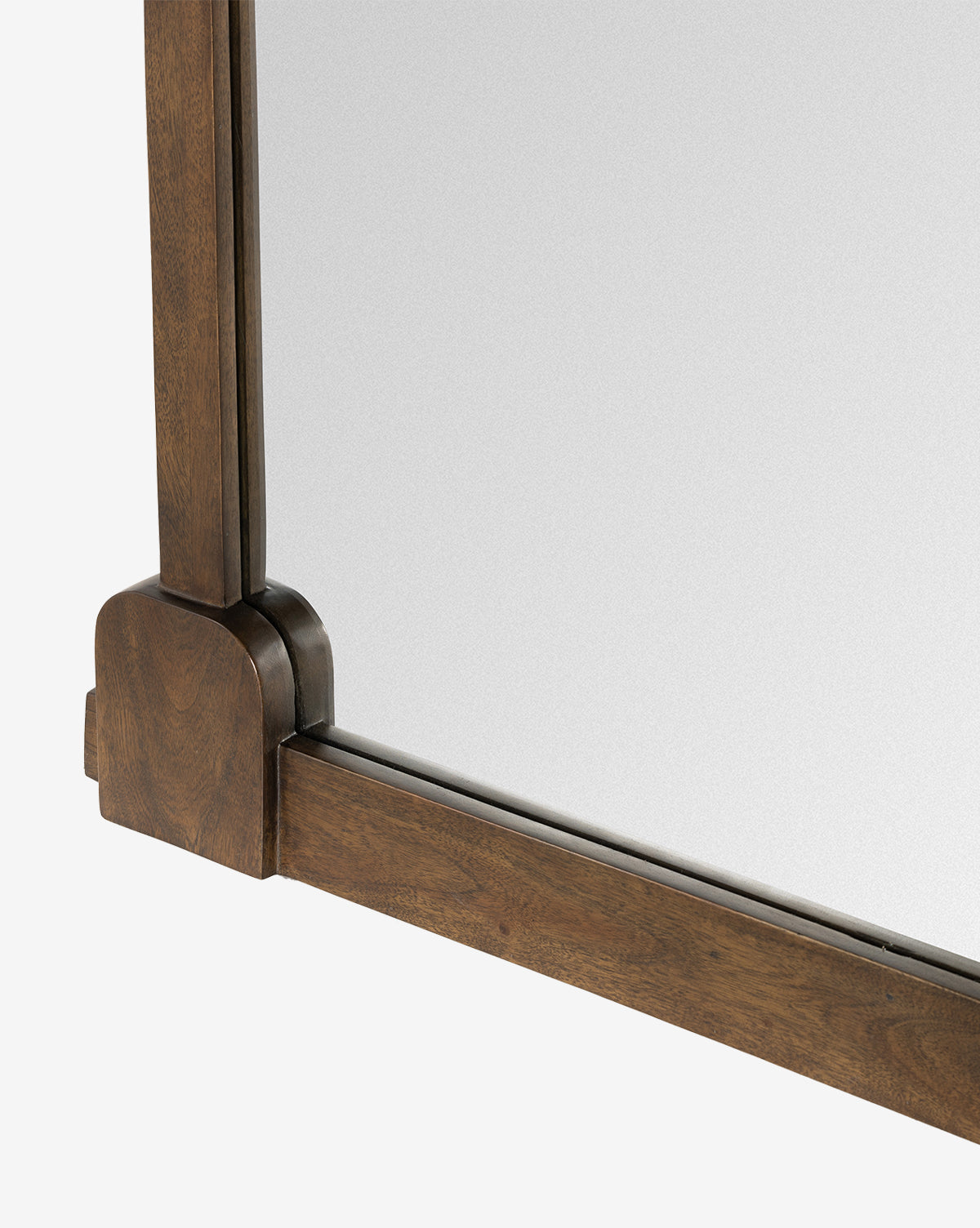 A close-up of the Letterly Floor Mirror’s bottom corner highlights traditional craftsmanship in its rich brown solid acacia wood frame and a portion of the reflective glass surface, by McGee & Co.