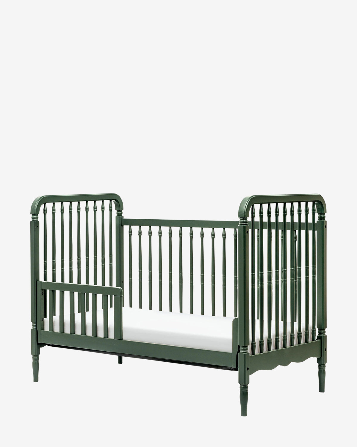 The Liberty 3-in-1 Convertible Spindle Crib in dark green features an open side and classic design, comes with a white mattress, and adapts to your child’s needs with an included toddler bed conversion kit, by McGee & Co.