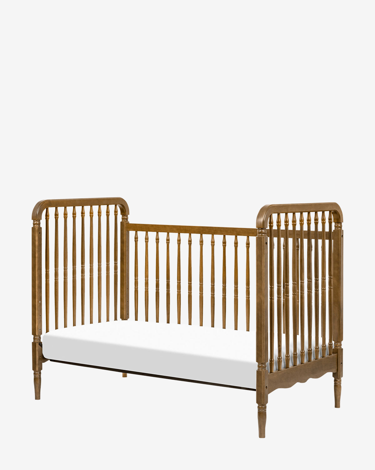 The Liberty 3-in-1 Convertible Spindle Crib with Toddler Bed Conversion Kit features classic vertical slats, an open front, white mattress, and vintage design. Easily converts to a toddler bed for lasting style and comfort as your child grows, by McGee & Co.