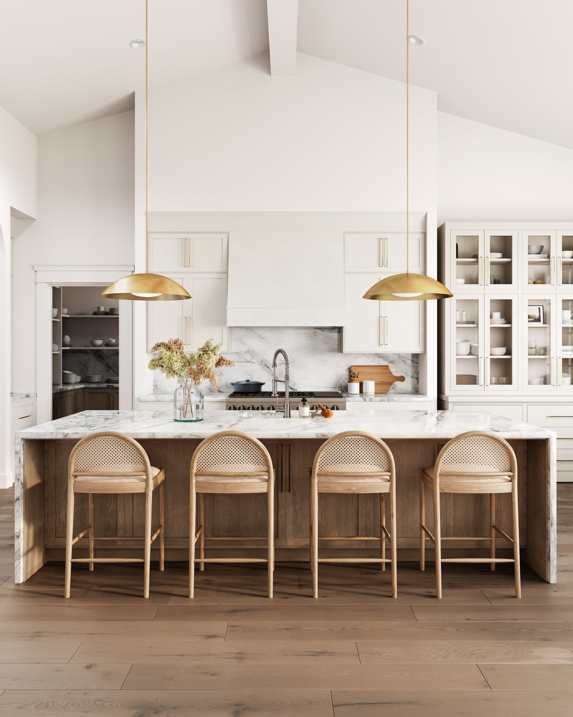 Modern kitchen with a marble island, four Hadden Natural Counter Stools with oak frames, brass pendant lights, white cabinetry, open shelving with dishes, and a vase of dried flowers. Sunlight highlights the coastal vibe, by McGee & Co.