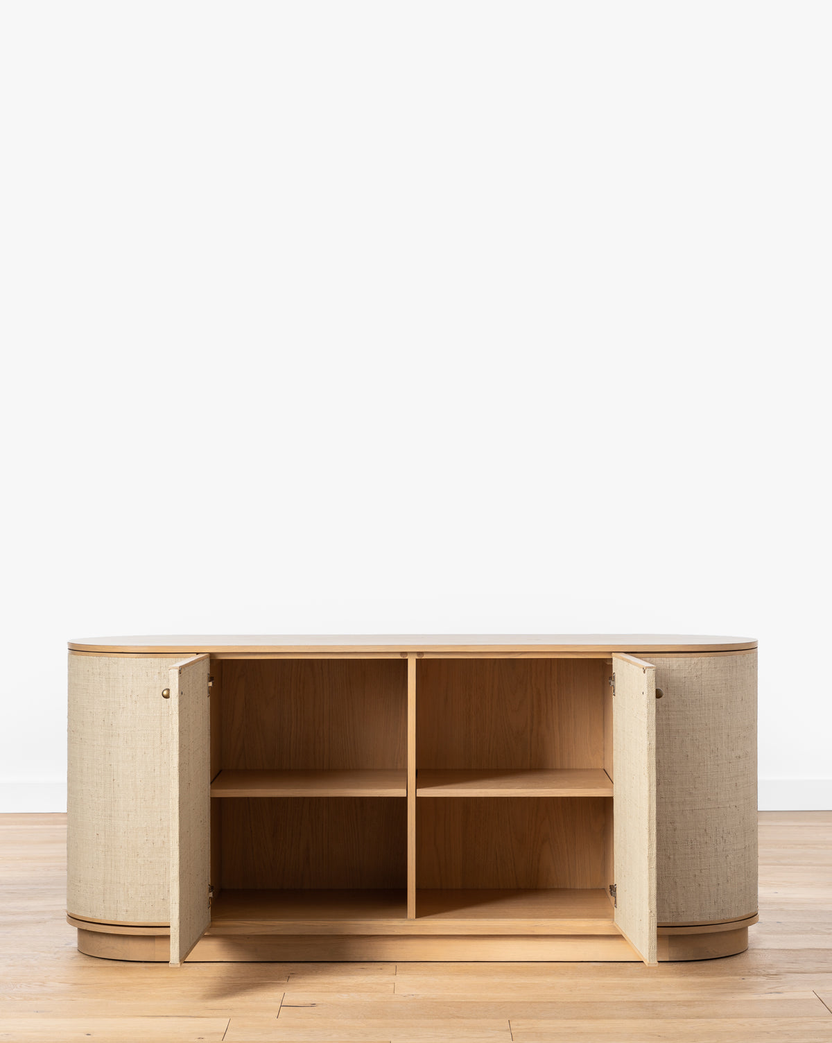 The Linu Woven Sideboard, with its light white oak frame, beige fabric-finished doors, and rounded corners, stands on a wooden floor. Two open doors reveal four spacious shelves against a clean white background, by McGee & Co.