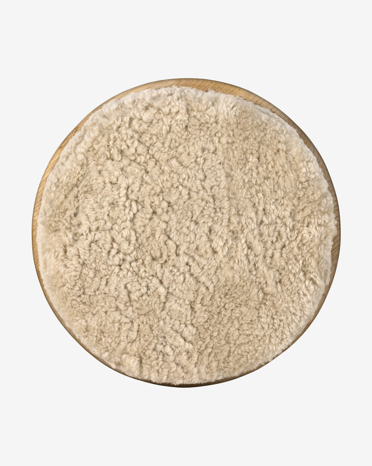 A round beige shearling wool cushion tops the Linus Stool’s wooden base, shown from above—ideal for cozy counter seating against a crisp white backdrop, by McGee & Co.