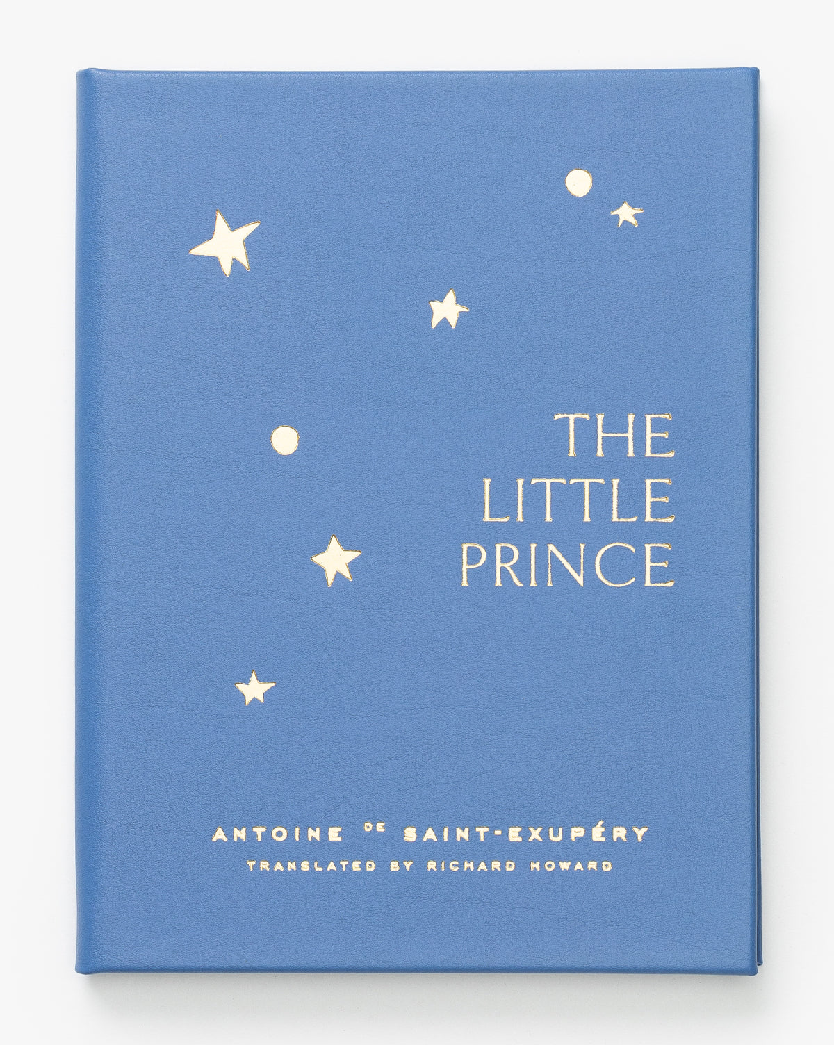 A blue children’s book cover with gold stars features the title Little Prince. Both author Antoine de Saint-Exupéry and translator Richard Howard are listed at the bottom, by McGee & Co.