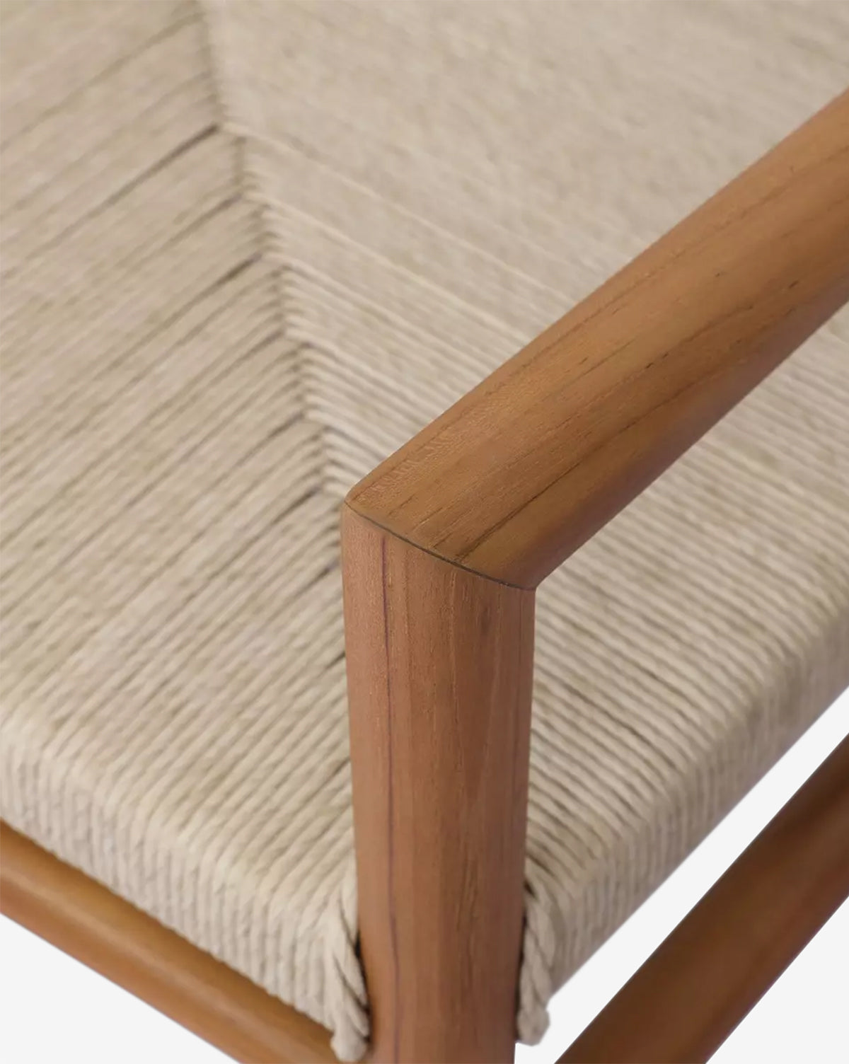 Close-up of the Lockridge Outdoor Chair shows its teak frame armrest and woven, light seat, highlighting the smooth wood grain and precise diagonal weave pattern, by McGee & Co.