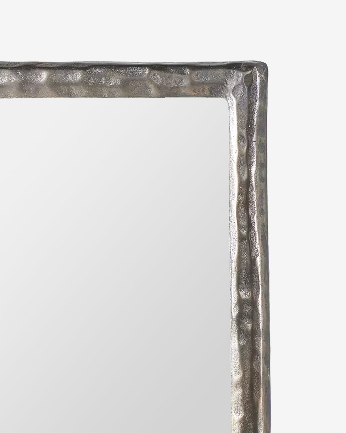 A close-up of the top right corner of the Lumi Wall Mirror, showcasing its textured, metallic hammered frame. The mirror’s surface is smooth and softly reflects light, by McGee & Co.