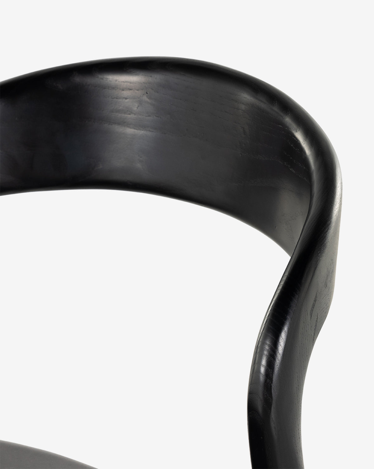 Close-up of the Lucinda Dining Chair’s smooth, curved black backrest against a white backdrop. Visible wood grain and a gentle arc showcase the elegant influence of Scandinavian design, by McGee & Co.