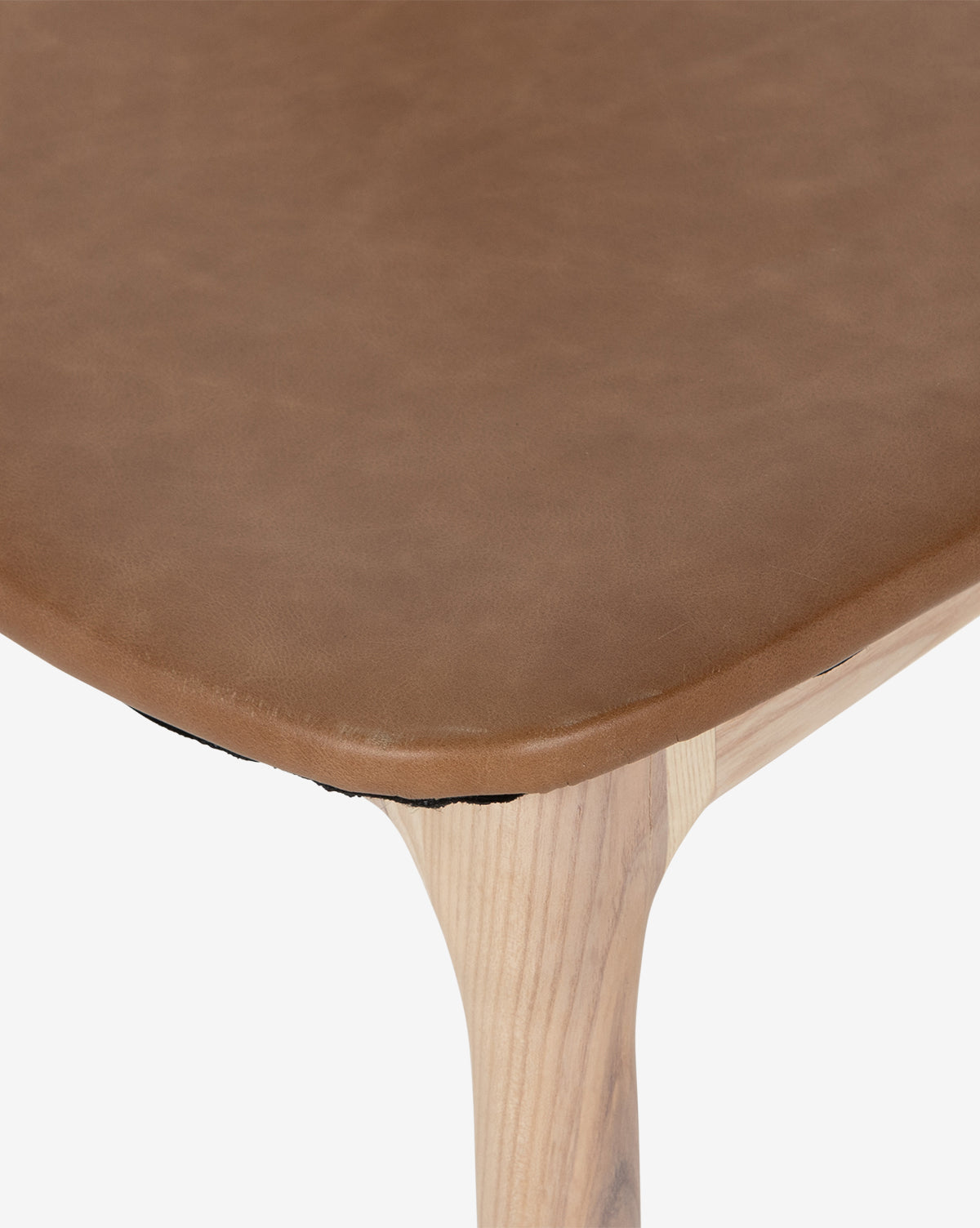 Close-up of the Lucinda Dining Chair seat featuring a brown top grain leather cushion and wooden legs, showcasing smooth texture and light wood grain inspired by Scandinavian design, by McGee & Co.