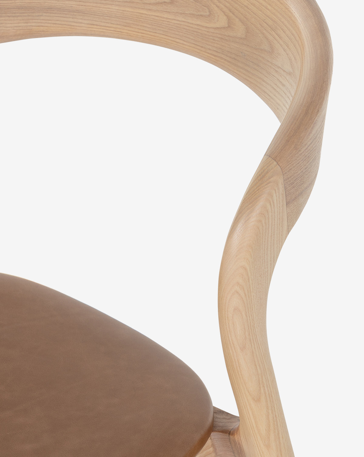 Close-up of the Lucinda Dining Chair, a modern Scandinavian design with a curved light wood backrest and brown top grain leather seat, shown against a plain white background by McGee & Co.