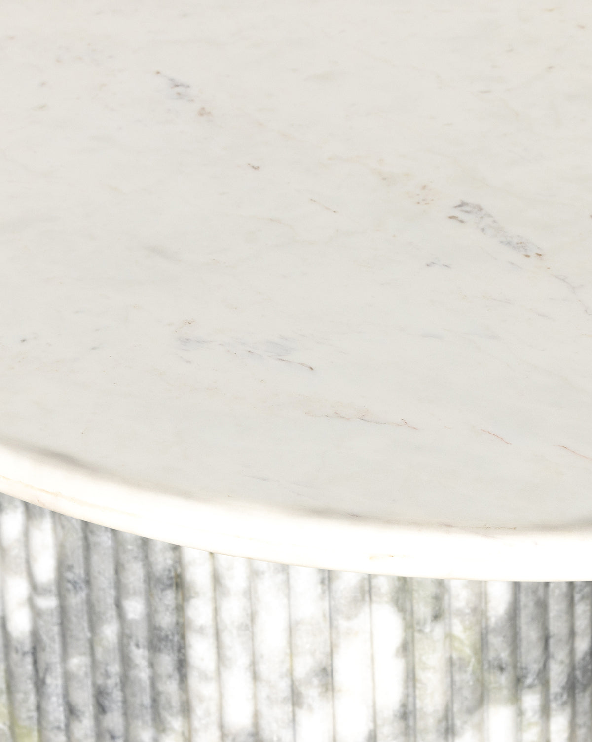 Close-up of the Patrick Dining Table, featuring a round white marble top with subtle grey veining on a vertically ribbed marble base, by McGee & Co. Shadows from nearby foliage highlight the table’s refined Italian-inspired contemporary design.