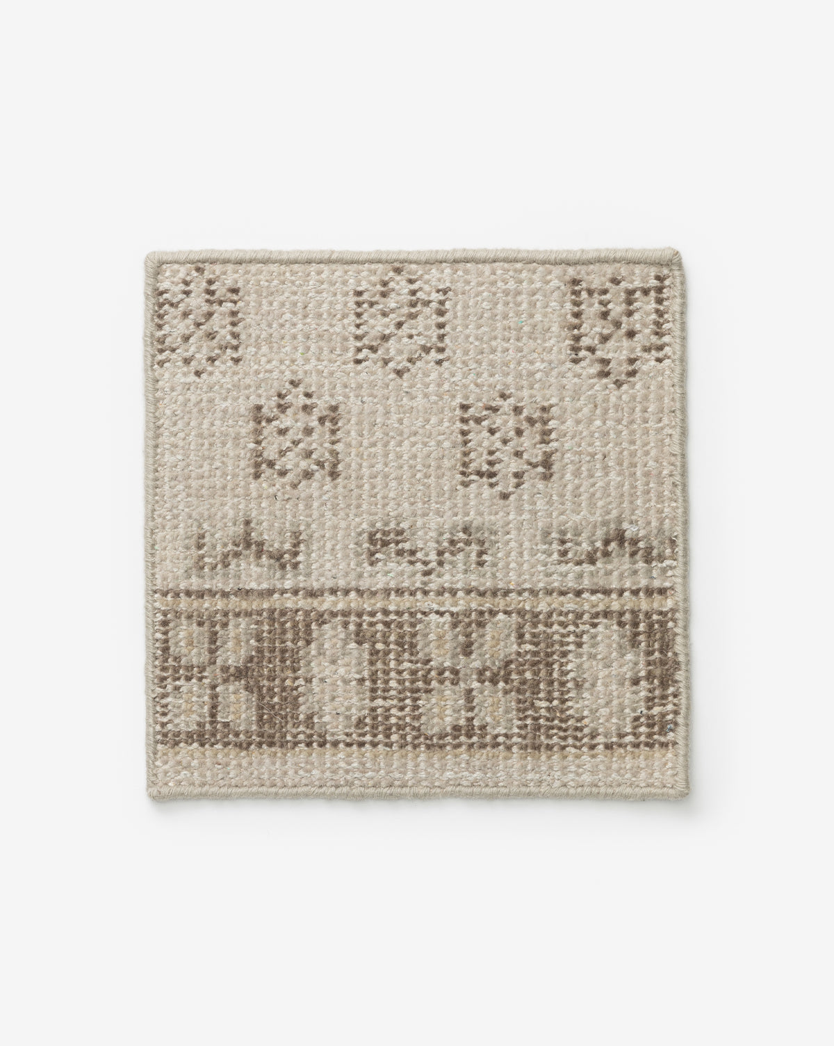 The Anya Hand-Knotted Rug Swatch is a rectangular wool sample in neutral tones, featuring a textured geometric pattern and a decorative border on one edge by McGee & Co.