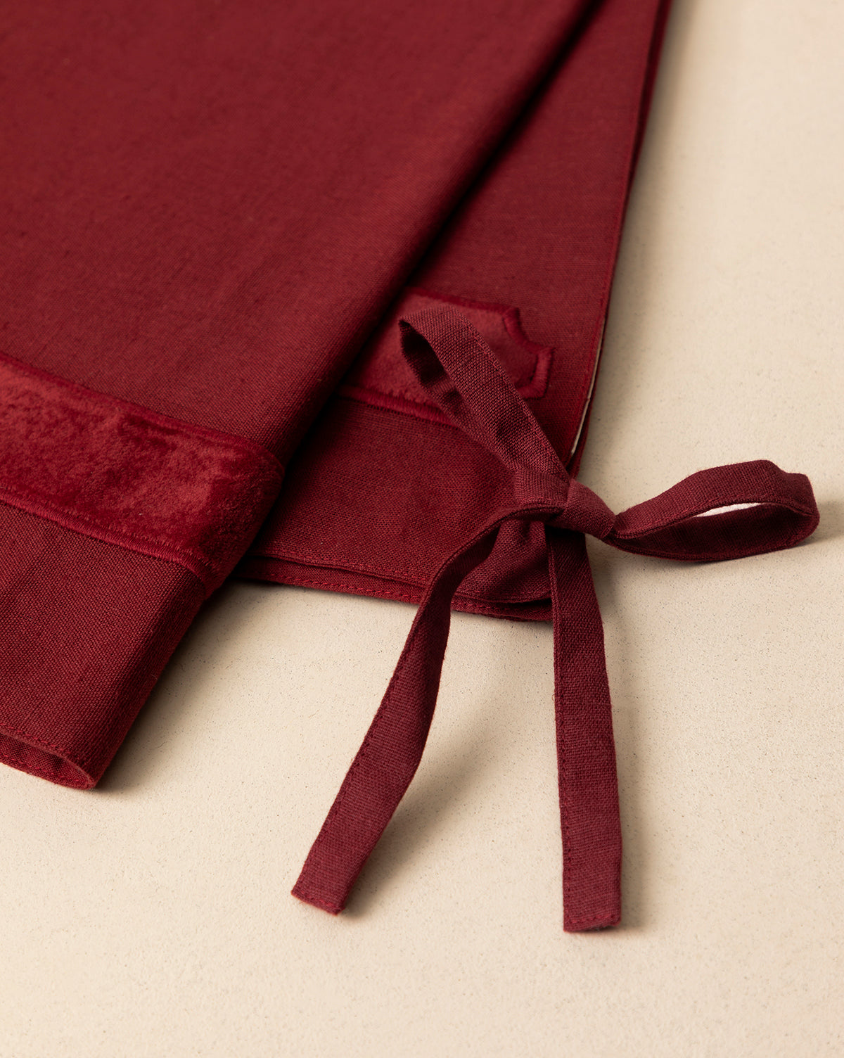 Close-up of the Mabry Velvet Trimmed Tree Skirt in deep red, folded on a light beige surface. The velvet texture and tie detail are clearly visible, by McGee & Co.